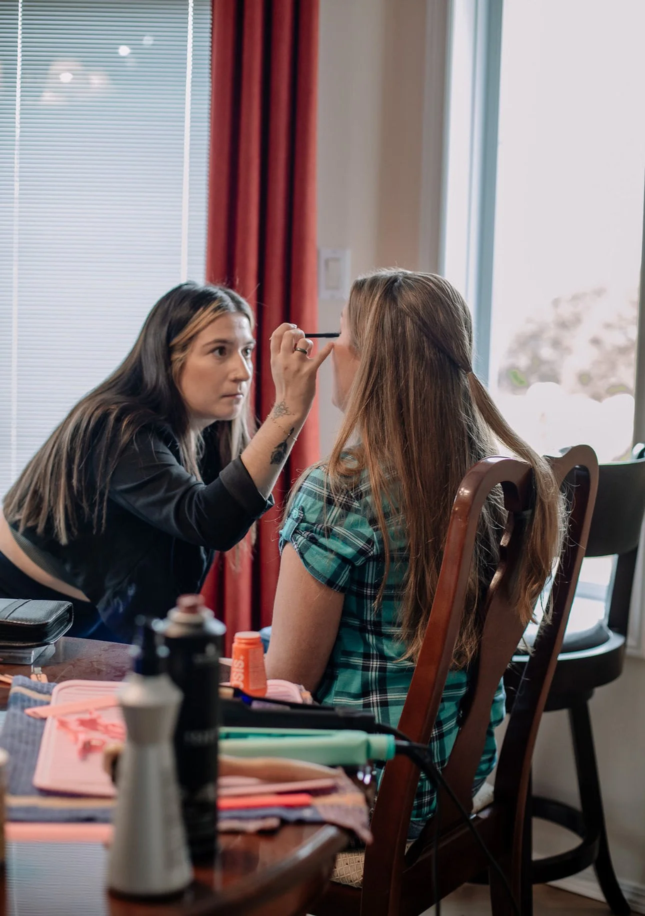 A woman sitting at a table gets her makeup done by a makeup artist.