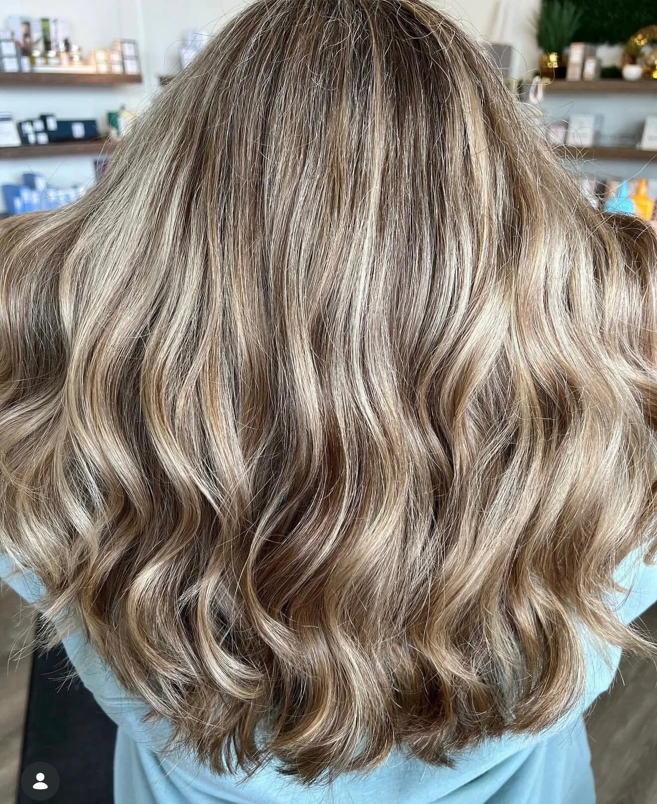 Back view of a woman with shoulder-length, blonde, wavy hair at a salon.