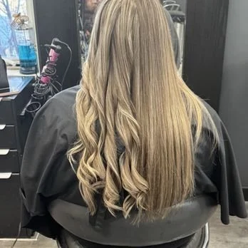 Back of a woman with long, blonde, curled hair sitting in a salon chair