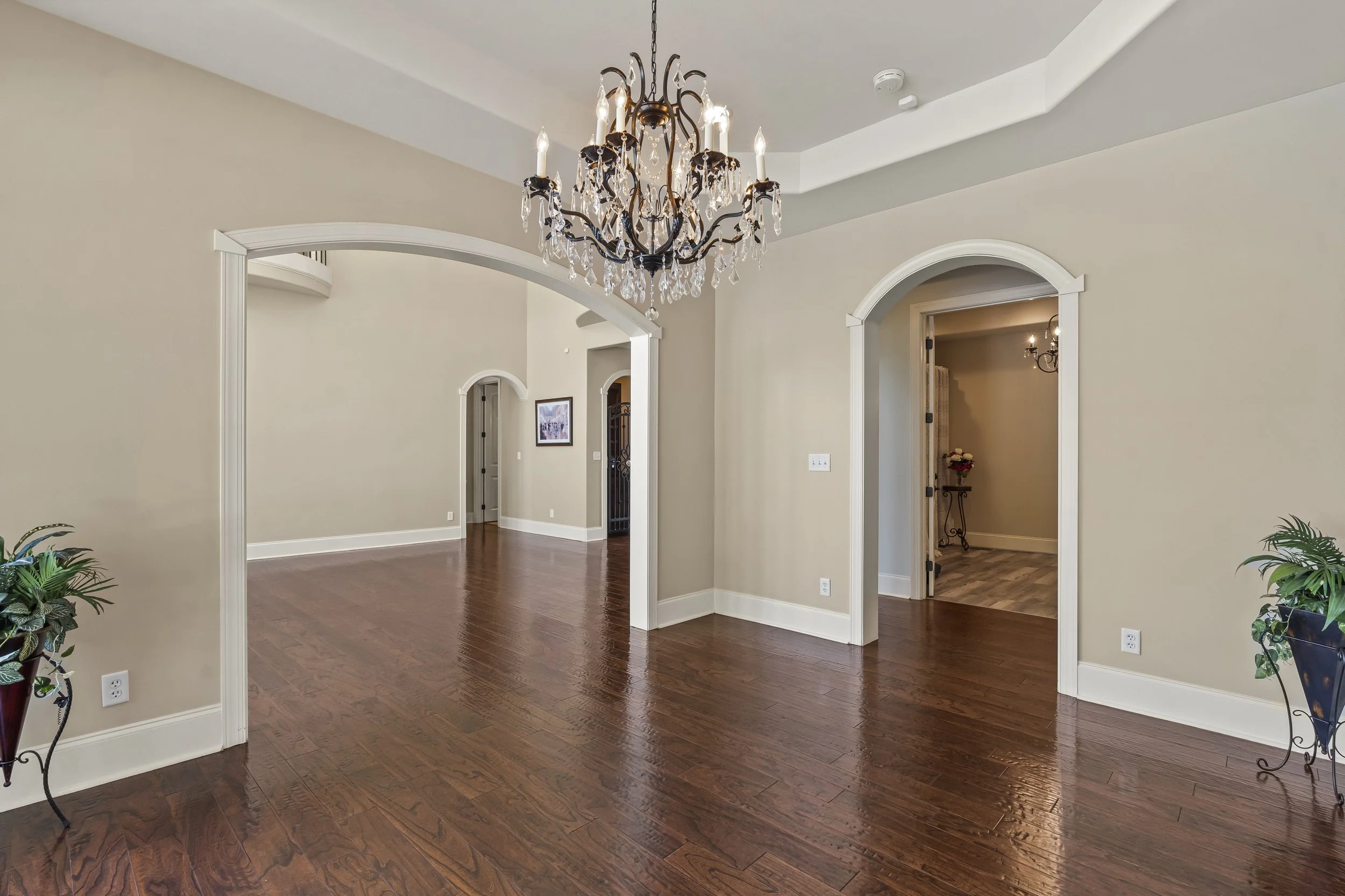 Interior of a home featuring a chandelier, hardwood floors, arched doorways, and beige walls.