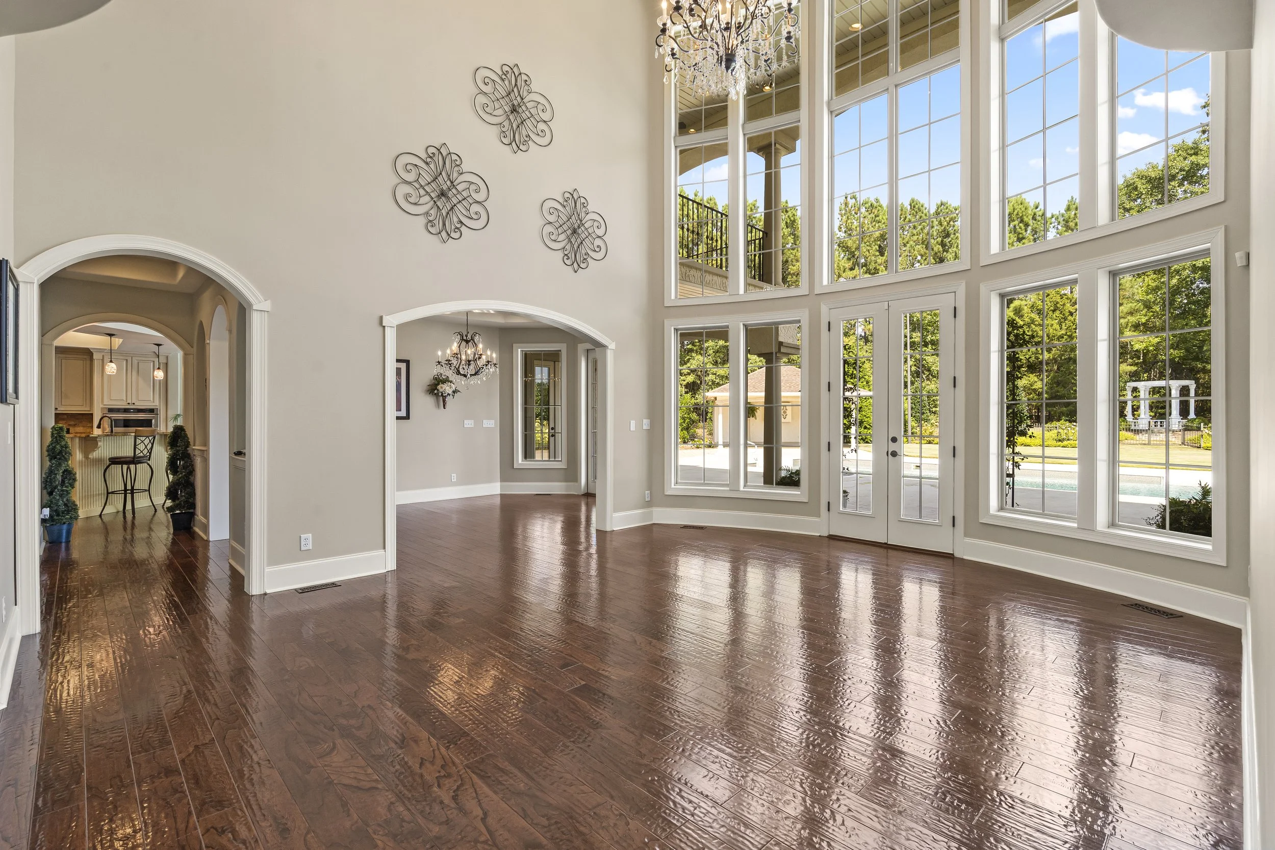 Spacious living room with large windows, hardwood floors, and chandelier, with view of backyard and pool
