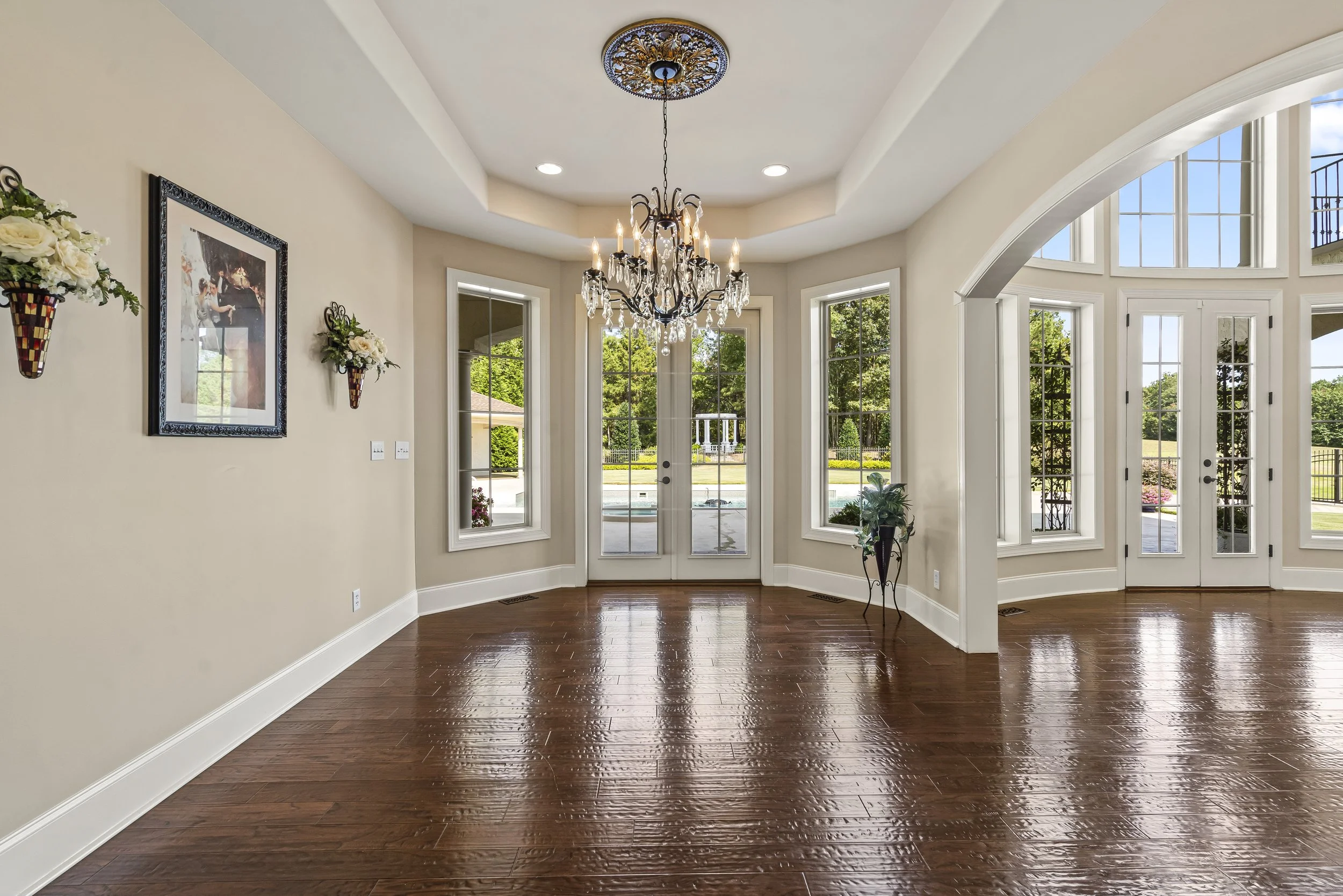 Bright living room with hardwood floors, white walls, a chandelier, large windows, and glass double doors leading outside.
