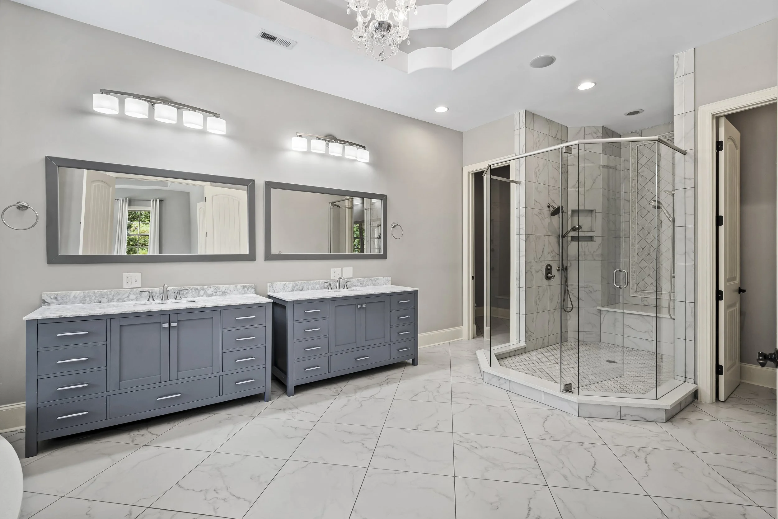 Modern bathroom with double vanity, marble countertops, two large mirrors, and a glass-enclosed shower with marble tiles.