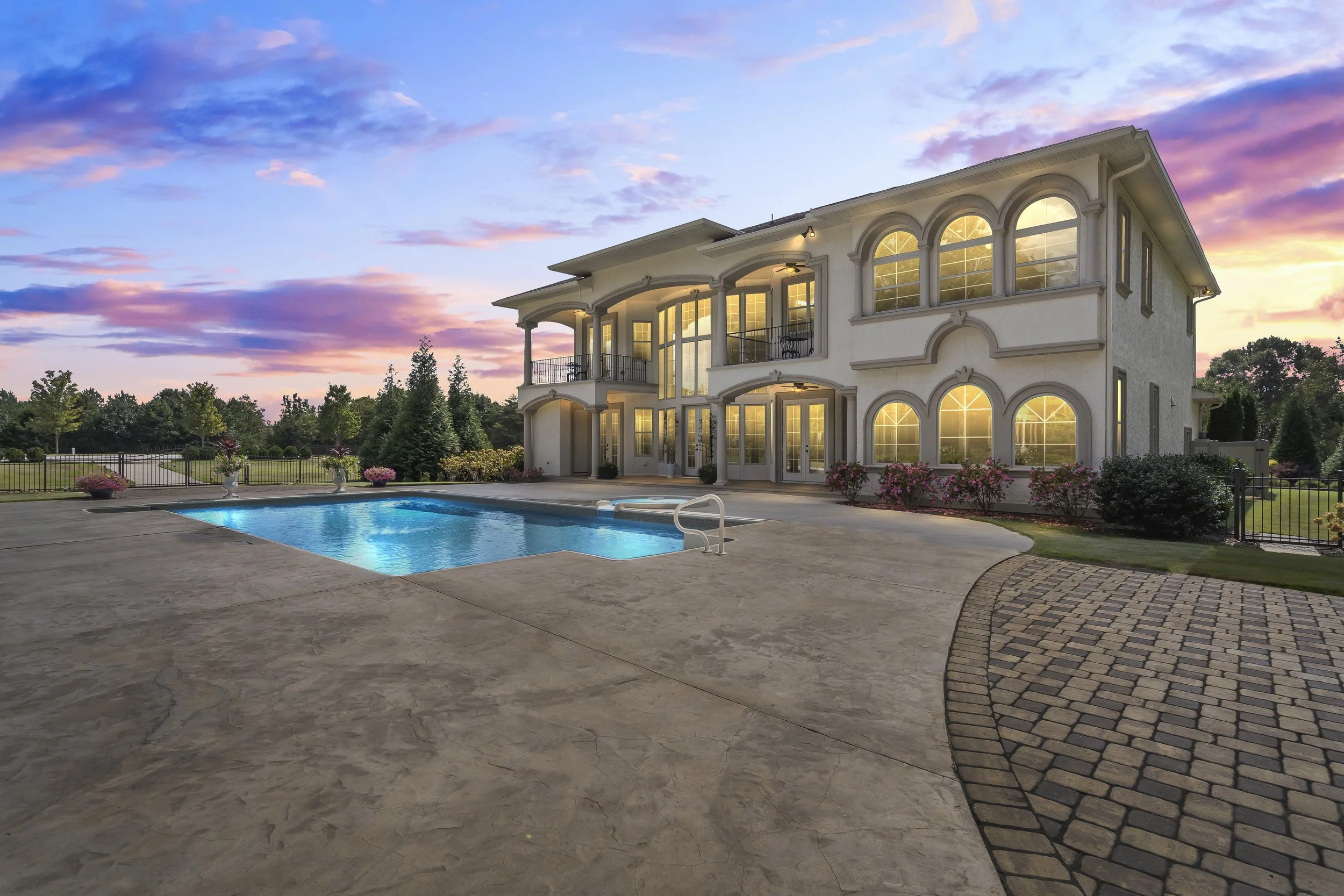 Large luxury house with illuminated windows and a swimming pool in the backyard during sunset.