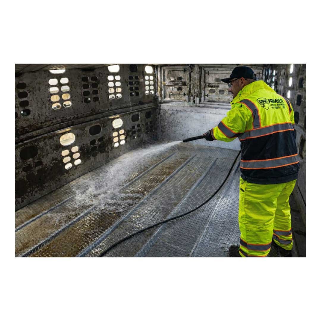 A worker in bright yellow and black safety gear pressures washing the interior of an airplane fuselage.