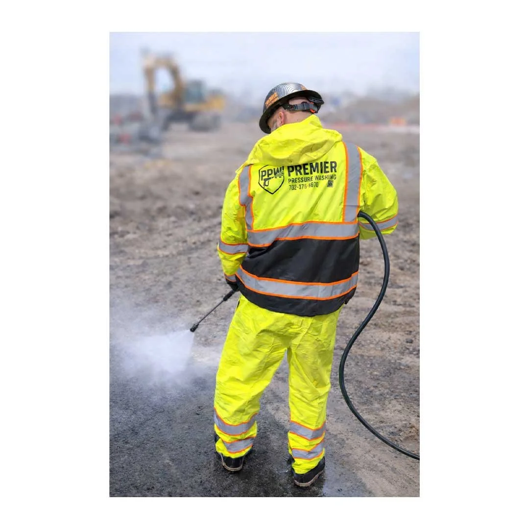 A construction worker in a bright yellow safety suit and helmet using a power washer on a construction site.