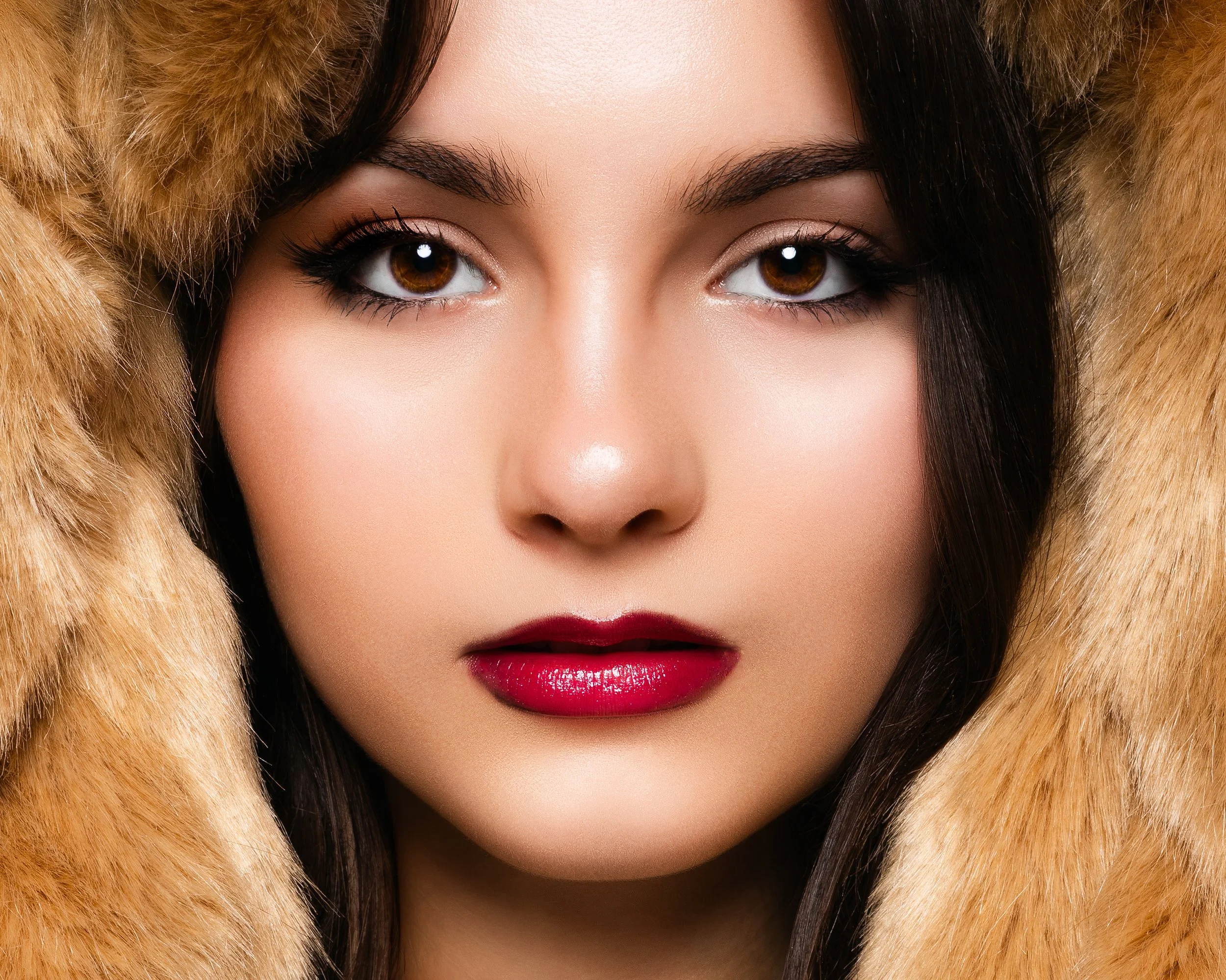 Close-up glamour shot of a woman with brown eyes, dark brown hair, red lipstick, and wearing a fur hood.