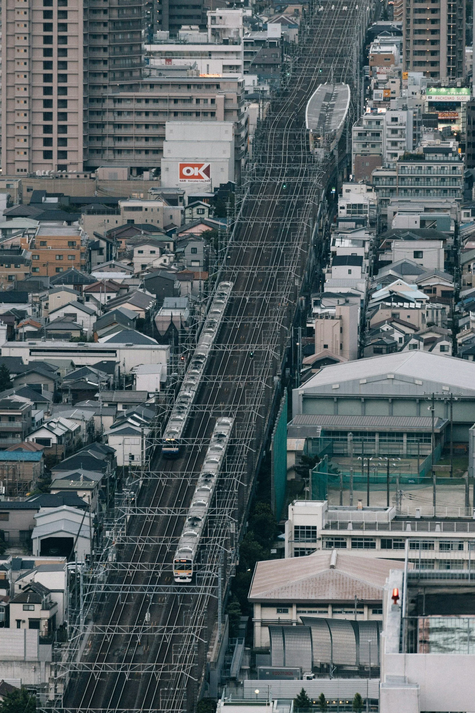 Cityscape featuring elevated train tracks with trains, surrounded by densely packed buildings and high-rise structures.