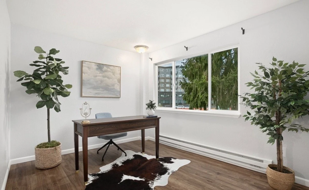 A modern office with a wooden desk, a light blue chair, a cowhide rug, potted plants, a large window showing a cityscape, and a wall painting of clouds.