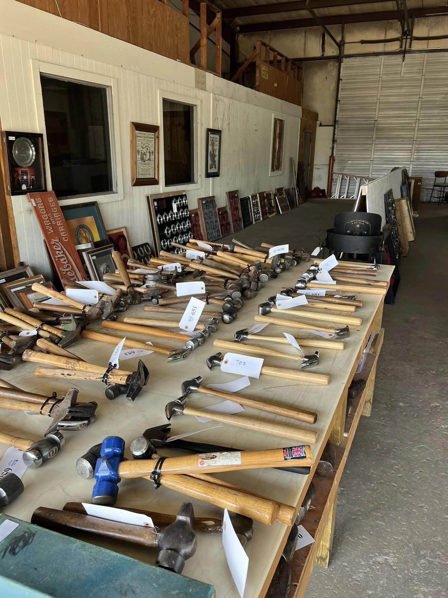 Assorted hammers and hand tools laid out on tables in a warehouse or storage space.