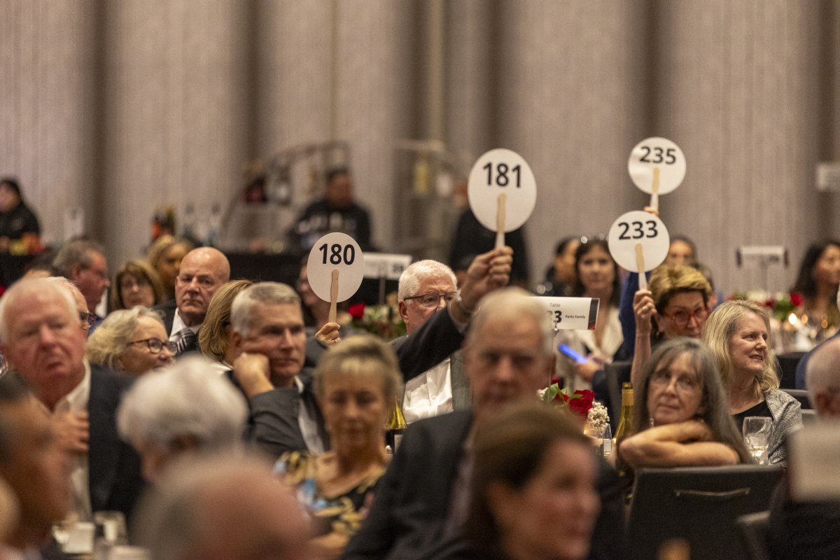 People sitting at a banquet table participating in an auction, holding up paddles with numbers, in a formal event setting.