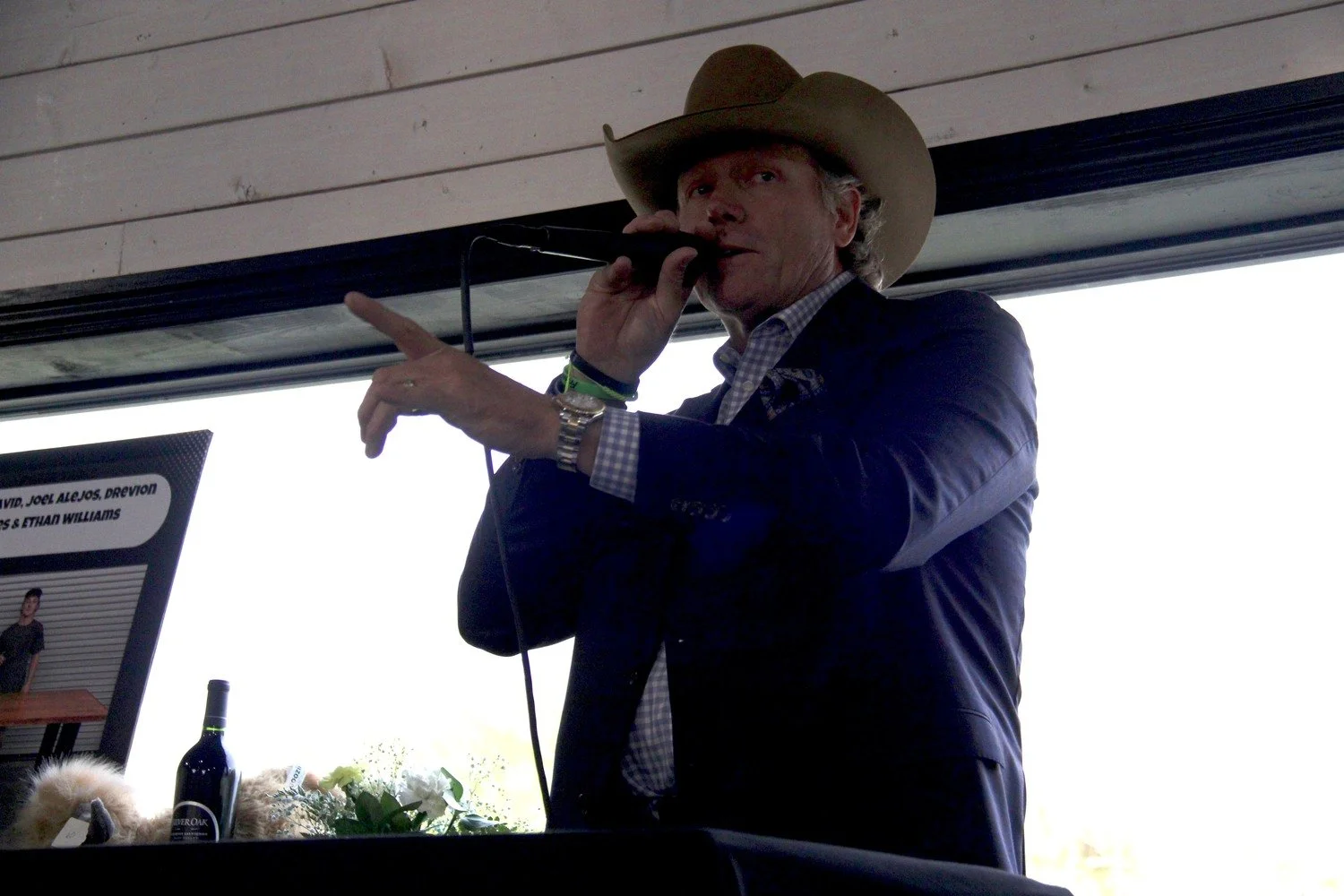 Man wearing cowboy hat speaking into a microphone at an indoor event