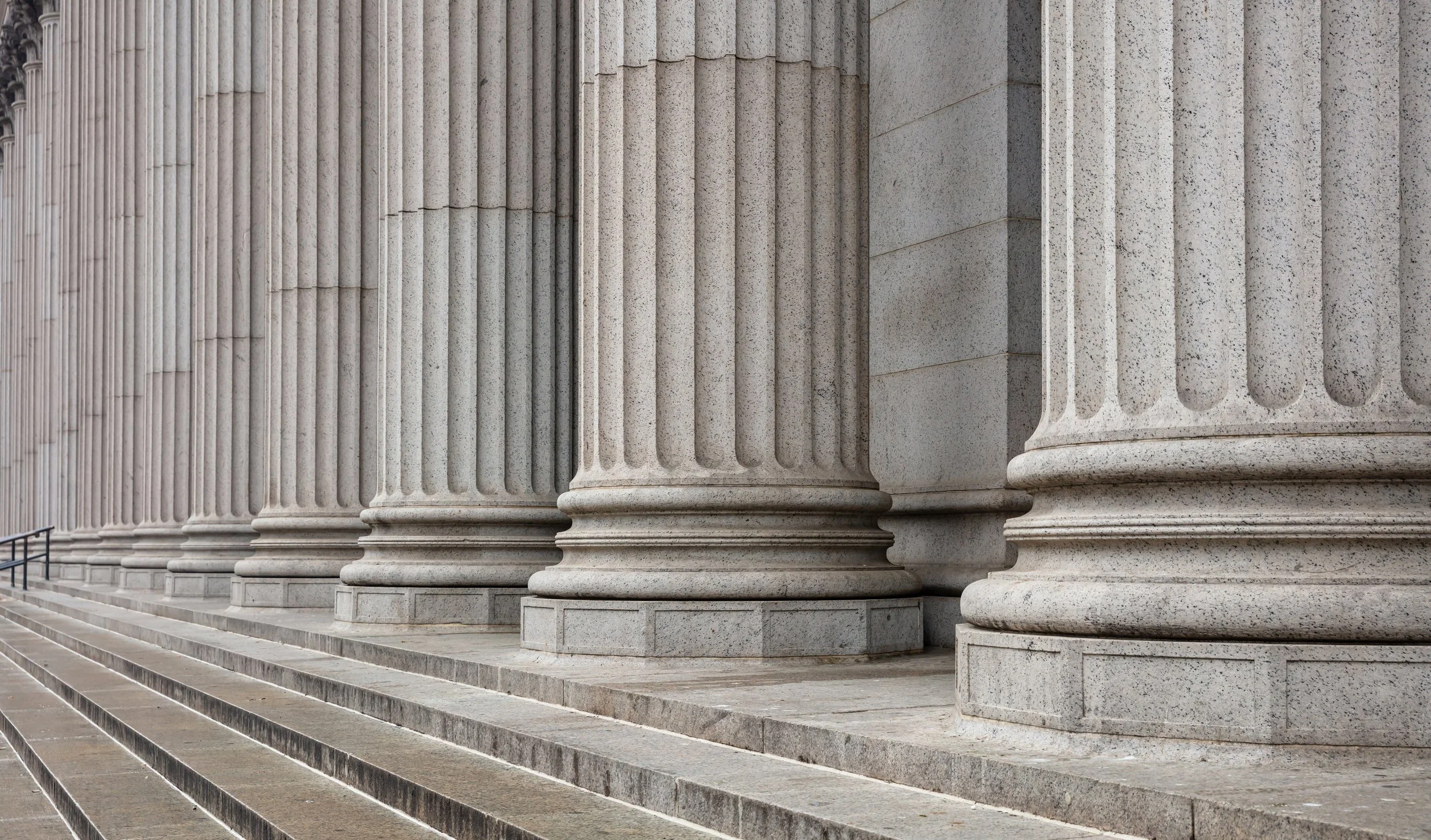 Close-up of large, classical stone columns with fluted shafts and rounded bases, part of a government or courthouse building, with stone steps in front.