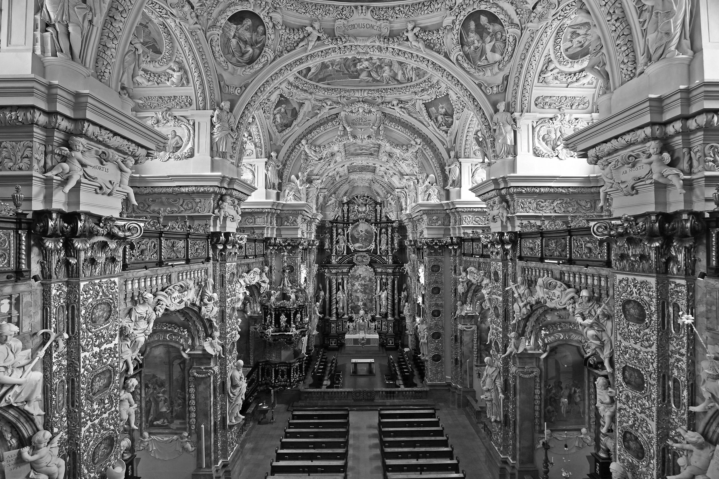 Innenraum einer Barockkirche mit barocker Einrichtung, viele Skulpturen, Gemälde und Verzierungen, zentrale Orgel im Hintergrund.