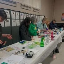 Four women standing at a table engaging in a craft activity in a room with posters on the wall.