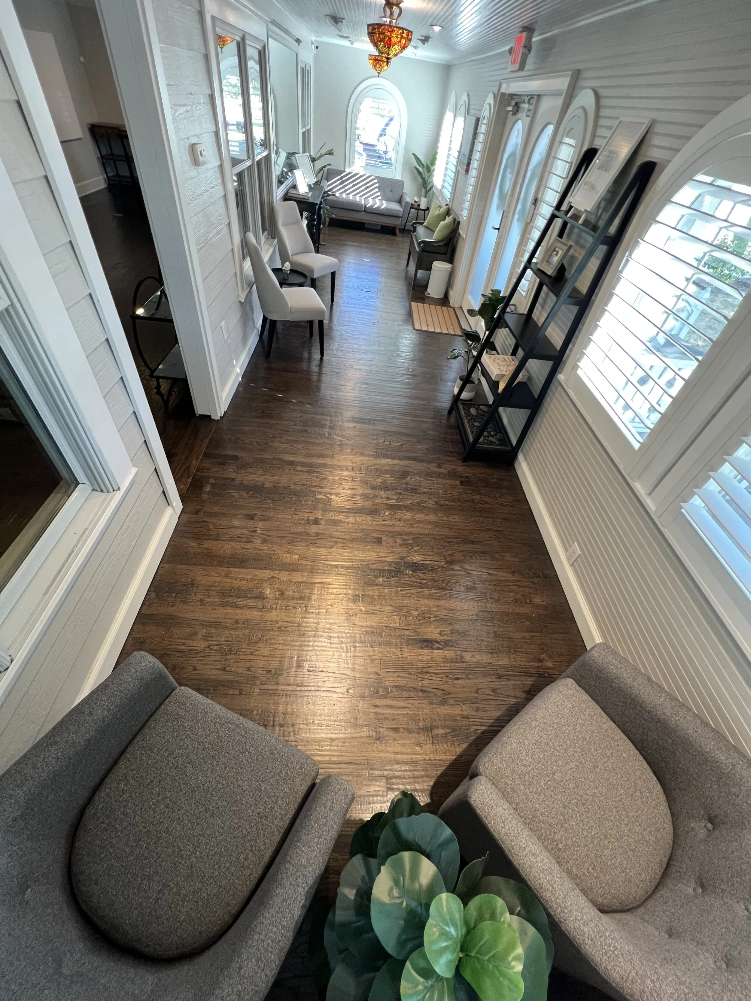 Healing House's bright, cozy lobby and waiting area or lounge with wooden floors, white walls with horizontal paneling, and large arched windows with plantation shutters.