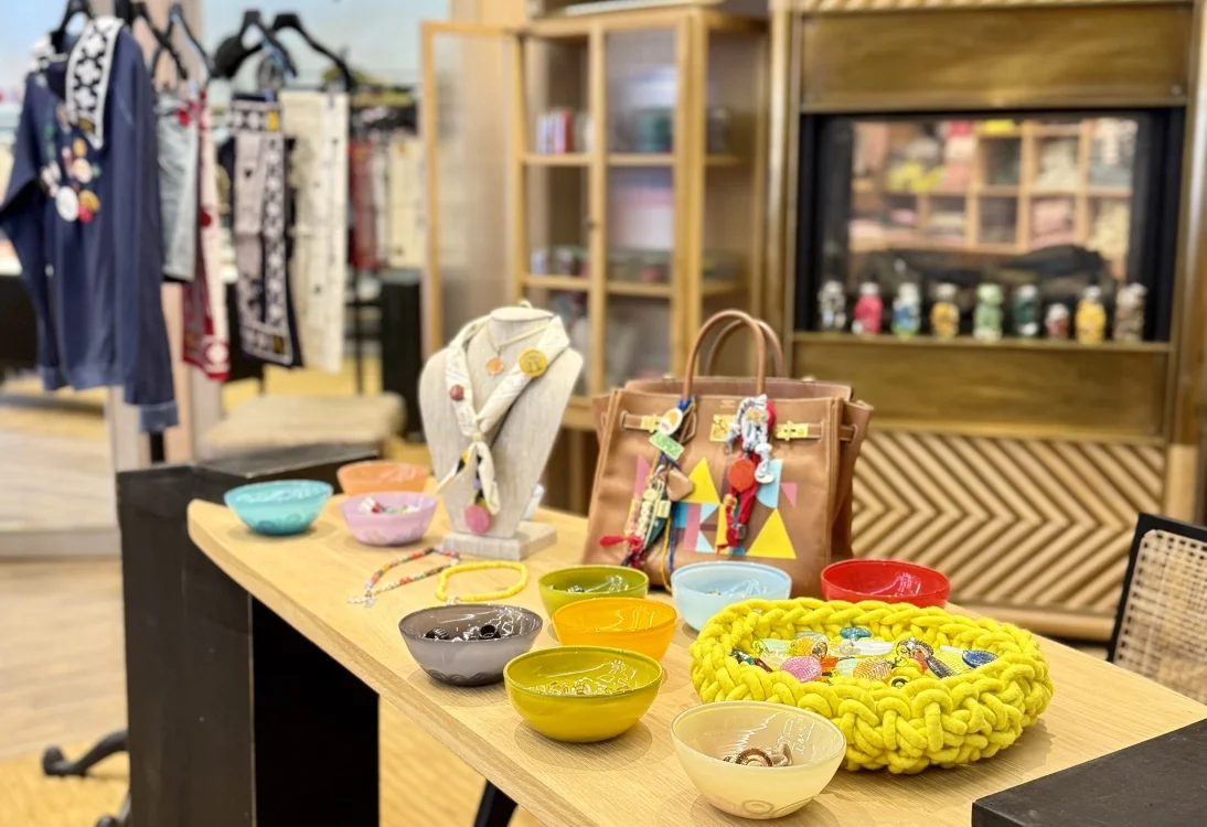 Display of colorful bowls, jewelry, and accessories on a wooden table in a boutique shop.