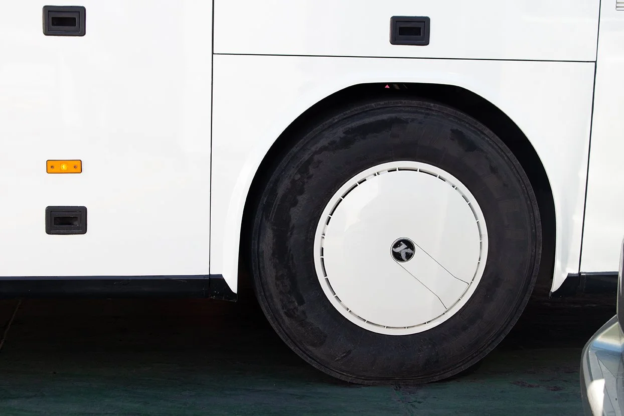 Close-up of a large white bus wheel and part of the bus body with black and orange reflectors.