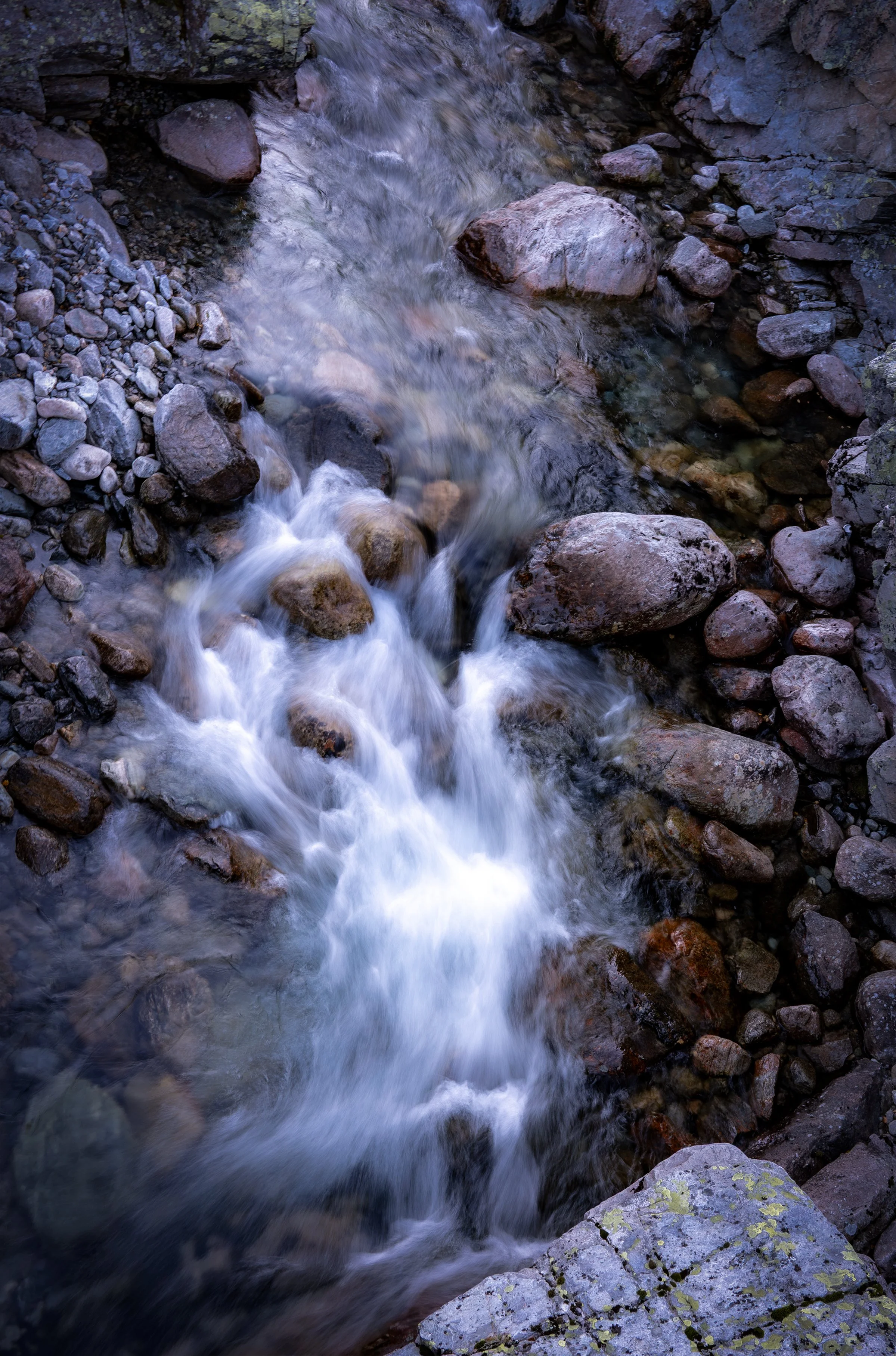 Stream flowing through a rocky terrain with smooth, rounded stones of various sizes and colors.