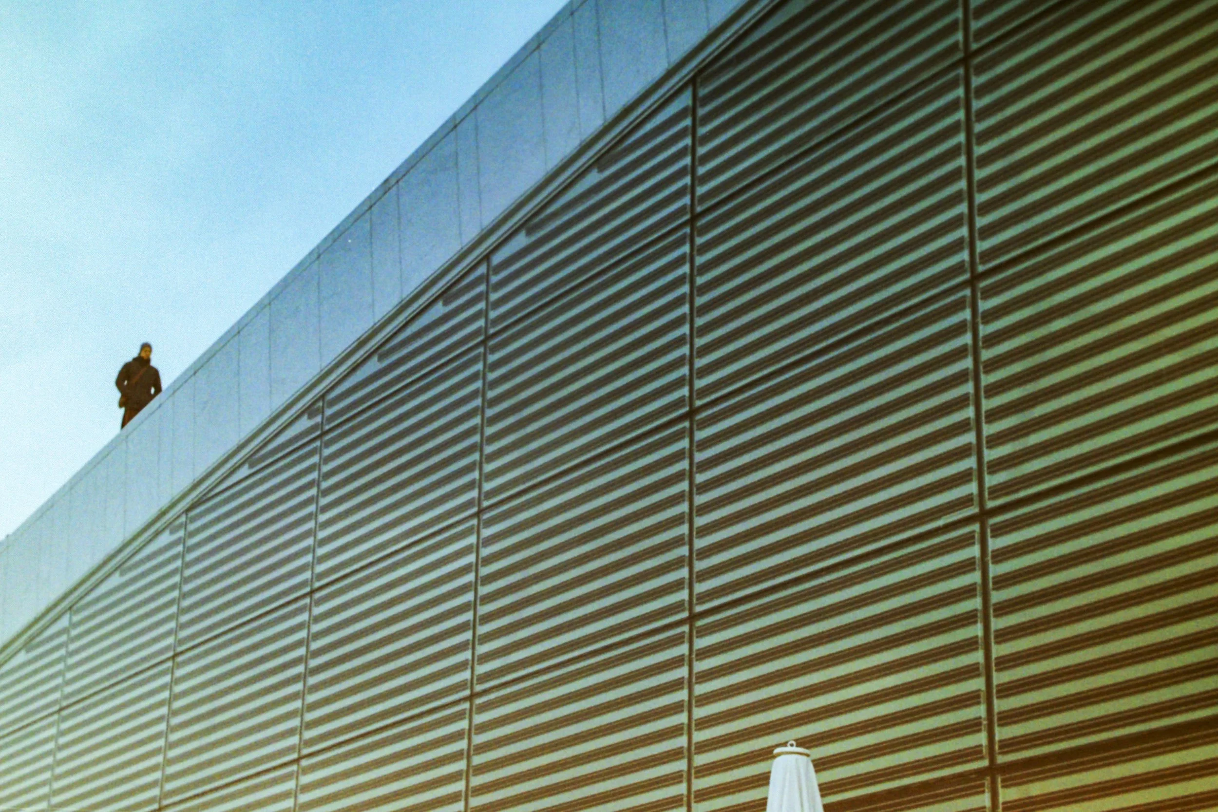 A person standing on the rooftop of a modern building with a facade of horizontal metal panels.