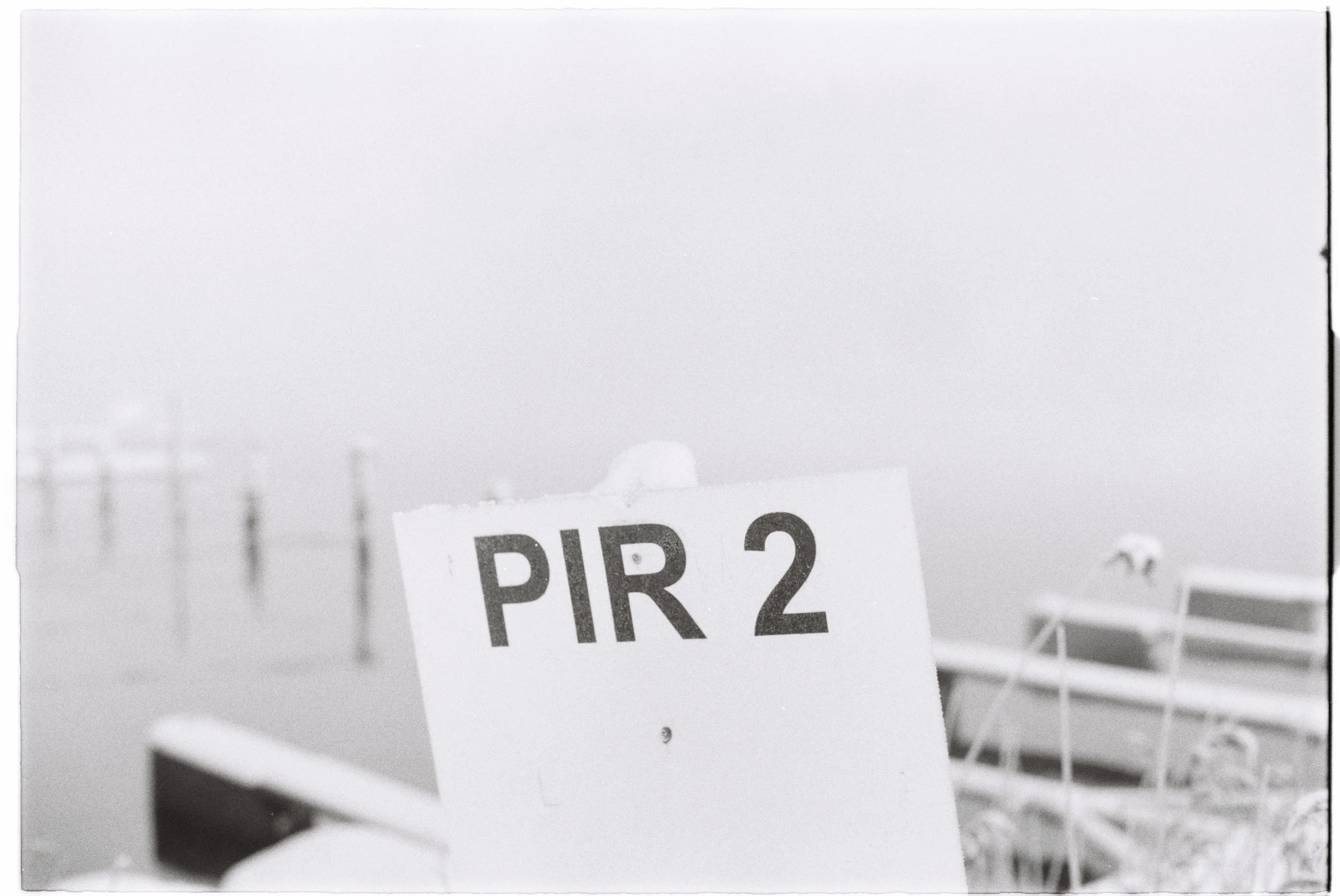 A boat docked near a body of water with a sign that reads 'PIR 2' in the foreground, and a foggy, indistinct shoreline in the background.