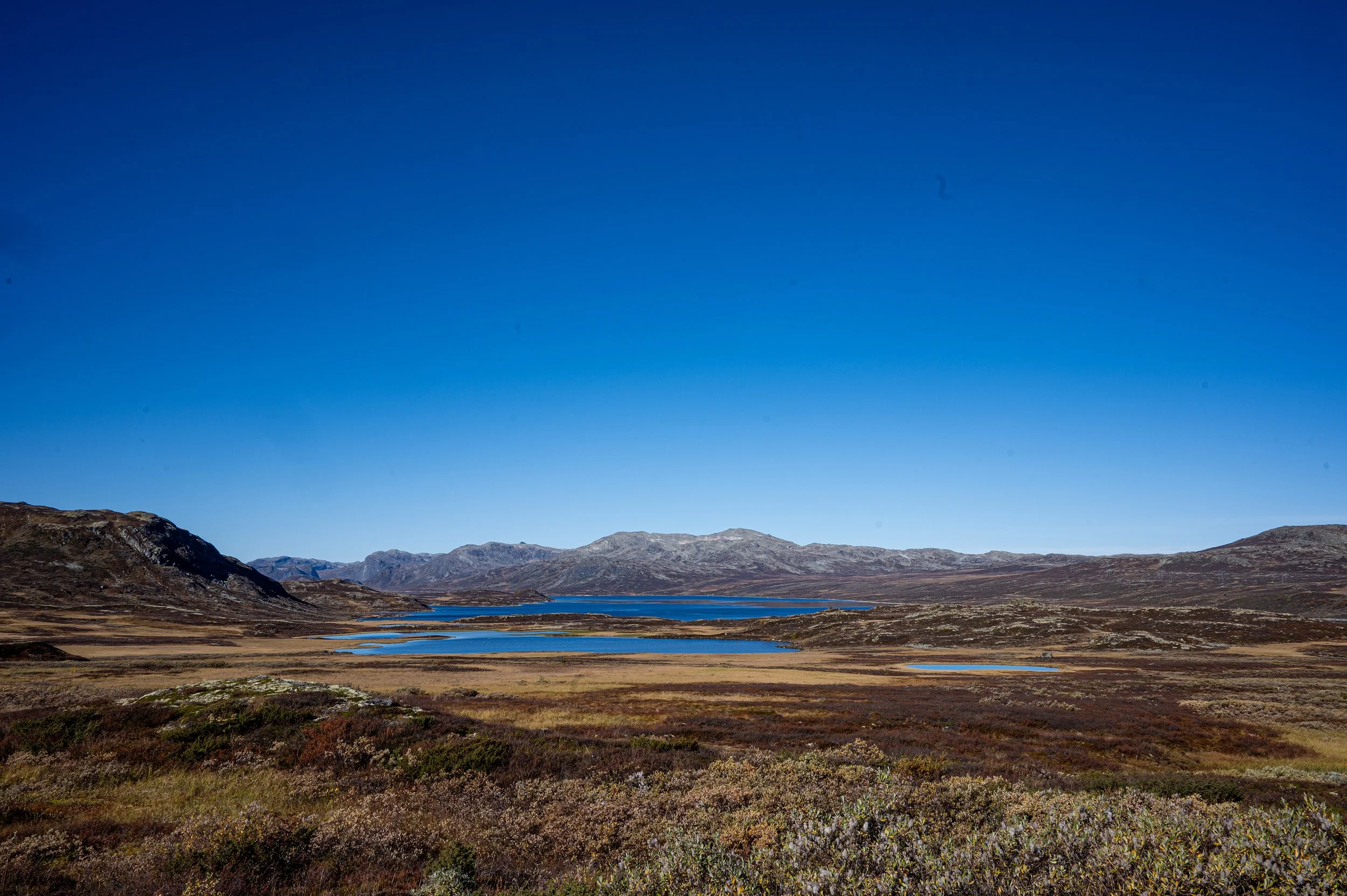 Scenic landscape of a valley with lakes, surrounded by rolling mountains under a clear blue sky.