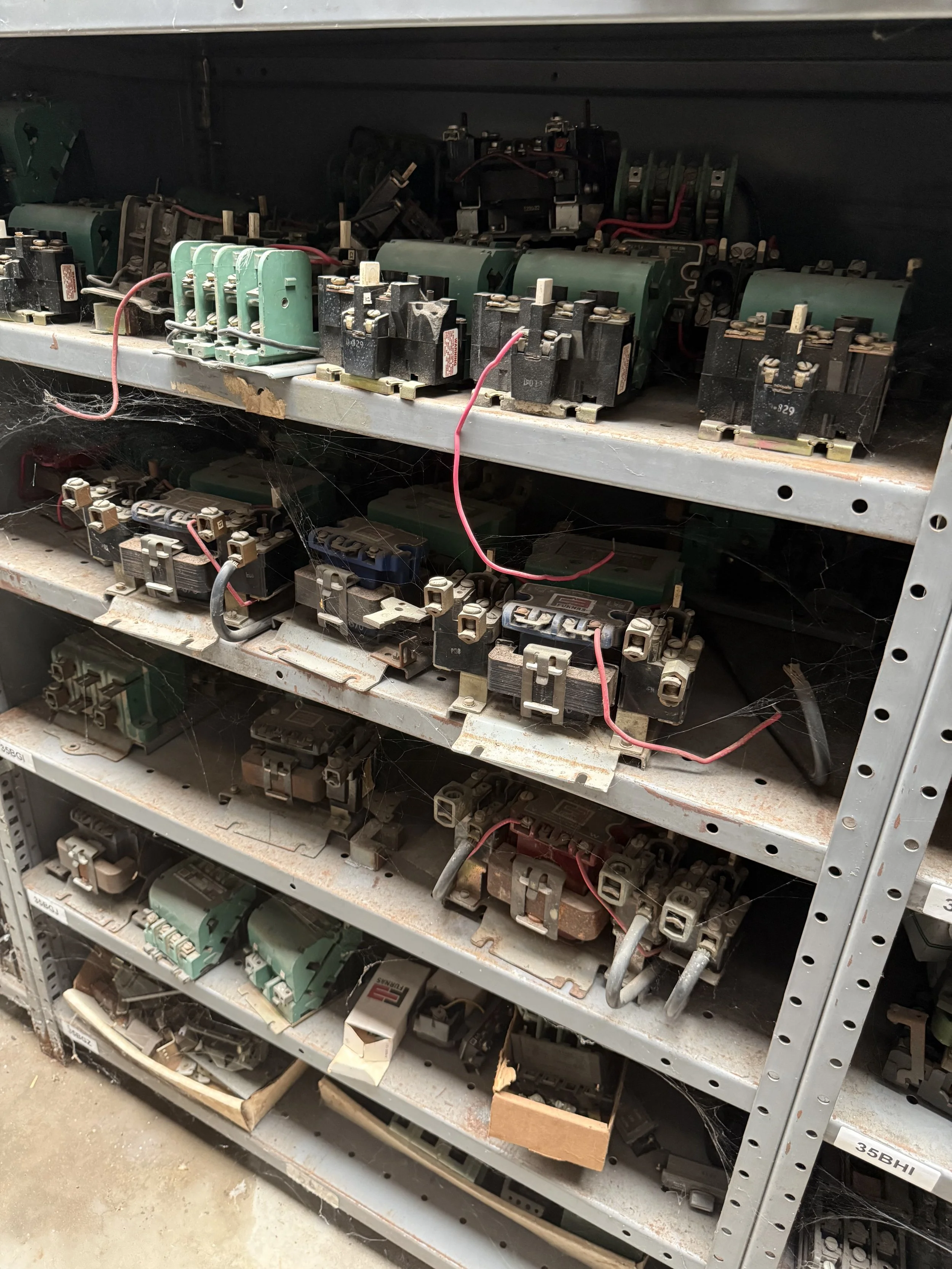 Metal shelf with various electrical components and relays, some with red and black wires. Vintage equipment, discontinued parts.