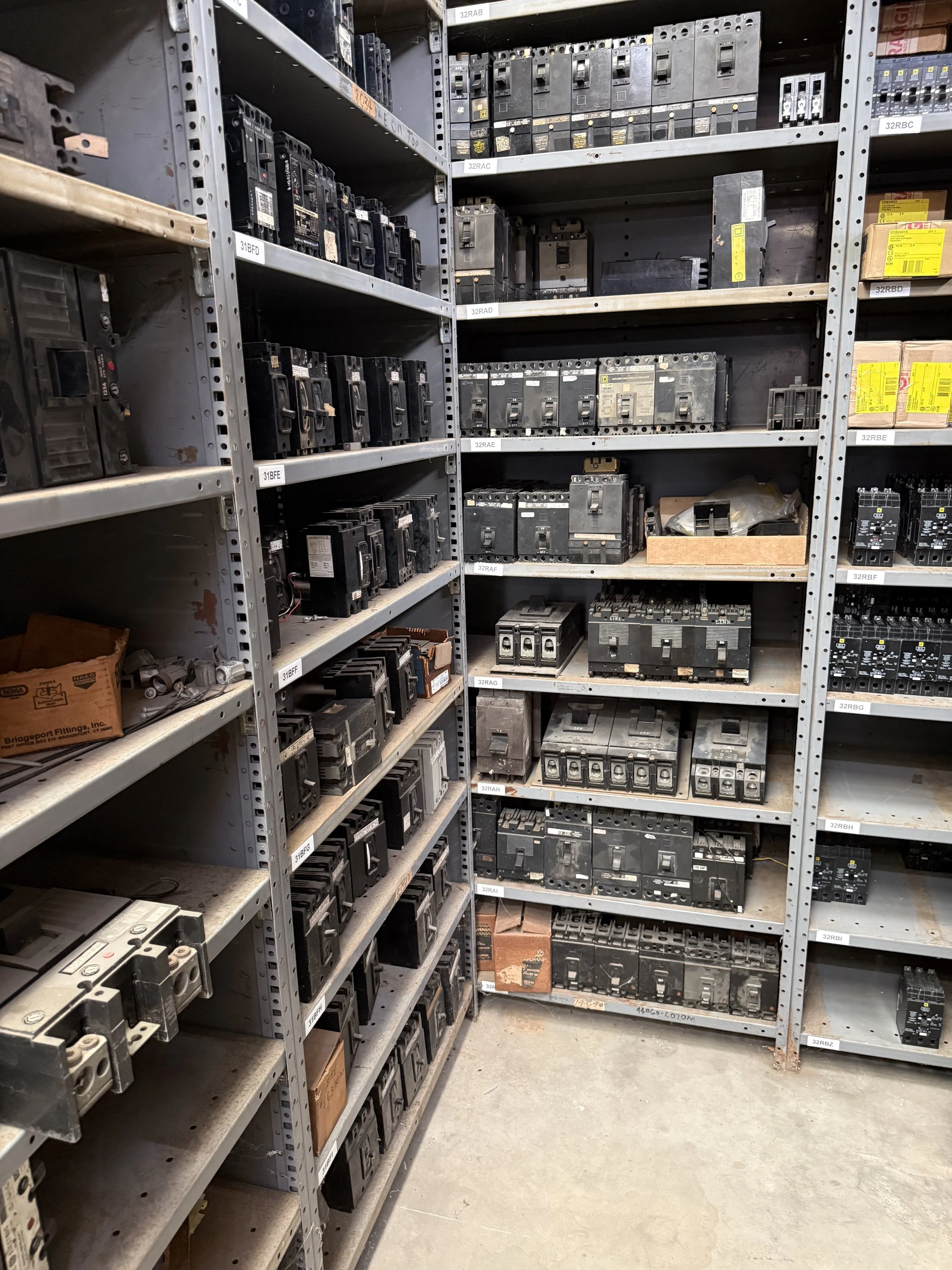 Metal shelving units filled with various electrical circuit breakers and electrical components
