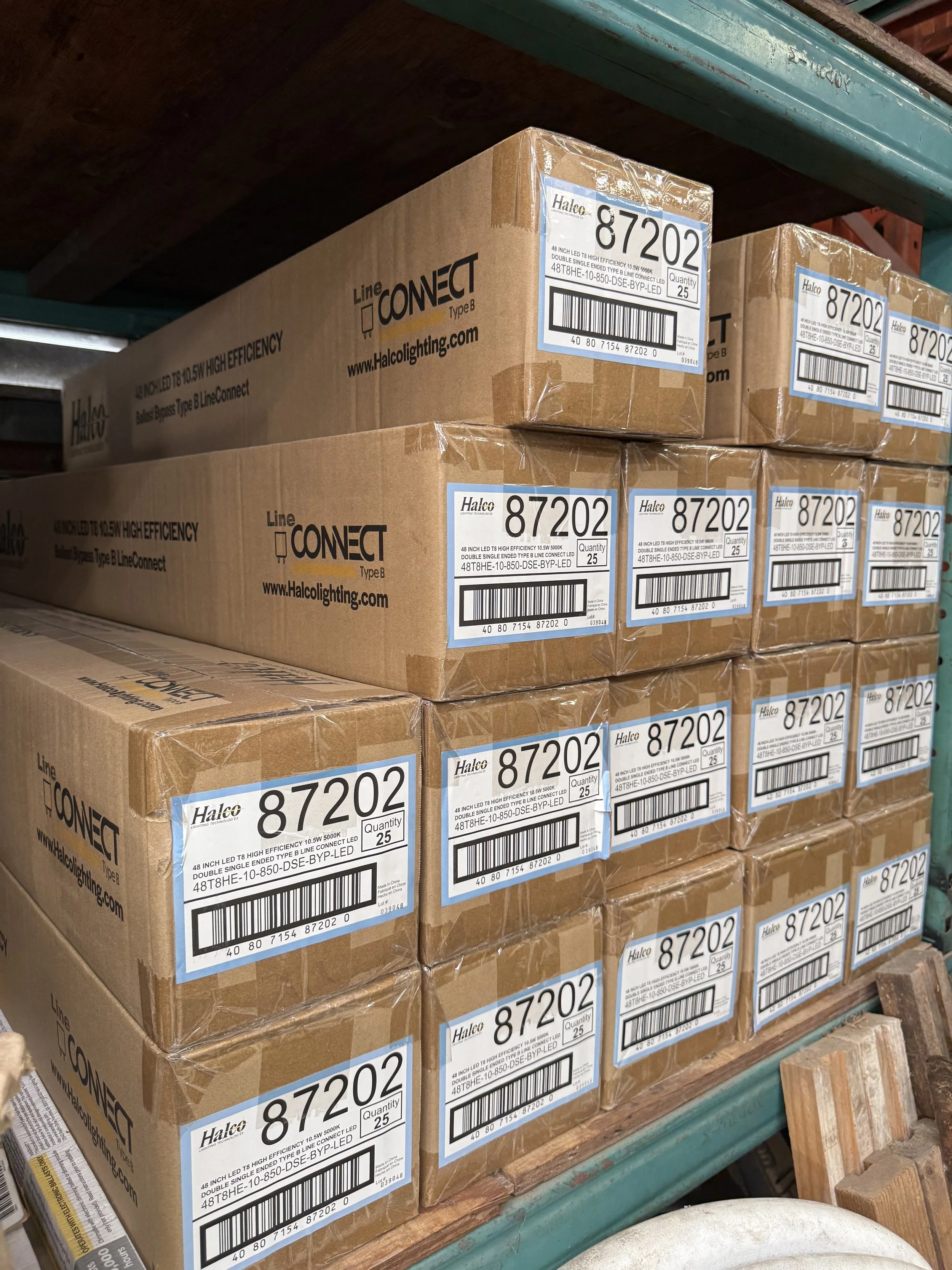 Stacked cardboard boxes labeled with the product number 87202, containing LED lighting strips, on a green metal shelf.