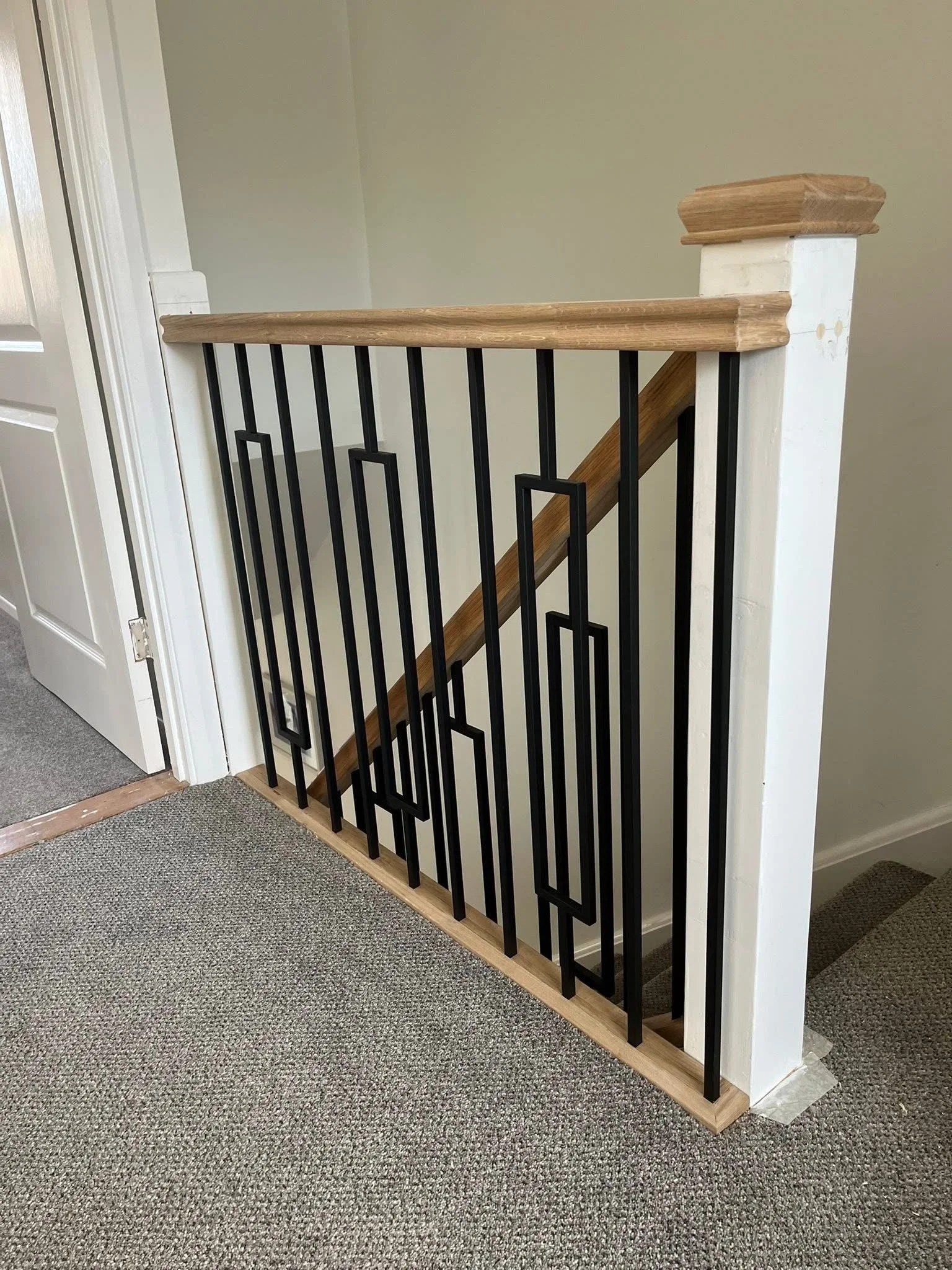 Modern black geometric spindles with oak handrail on a landing