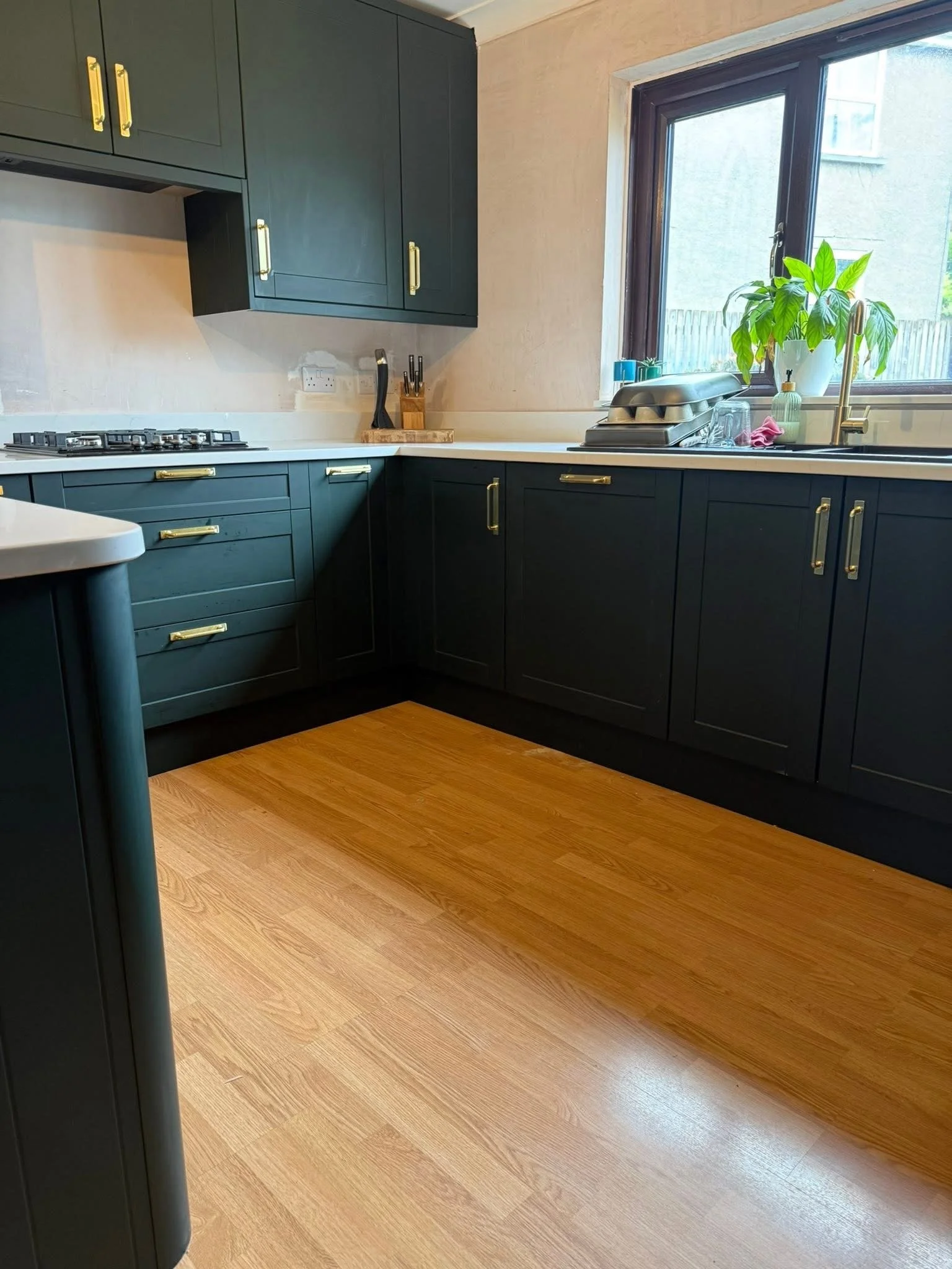 L-shaped green shaker kitchen with brass cup handles
