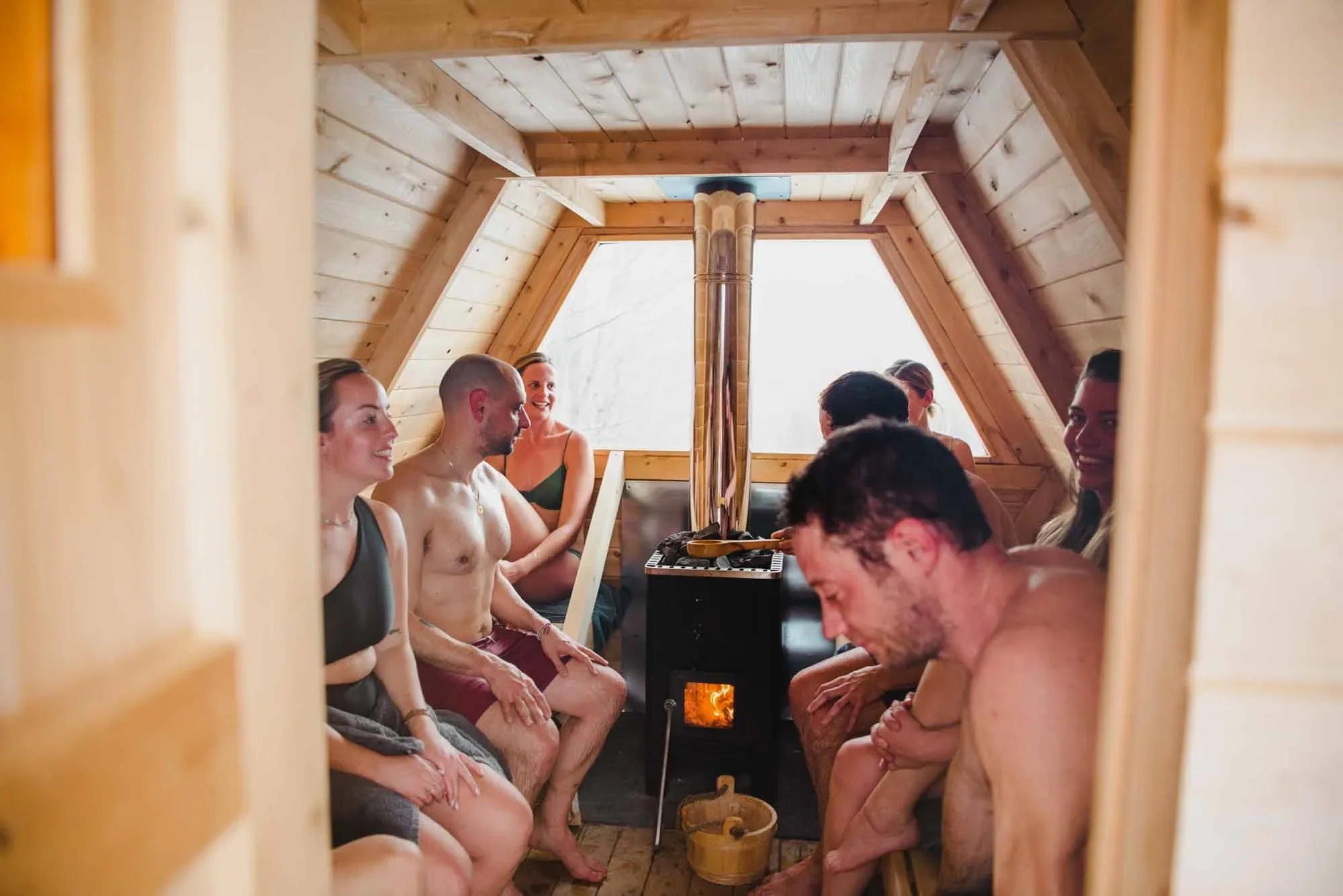 A group of people in a wooden sauna, sitting on benches, smiling, and enjoying the heat.