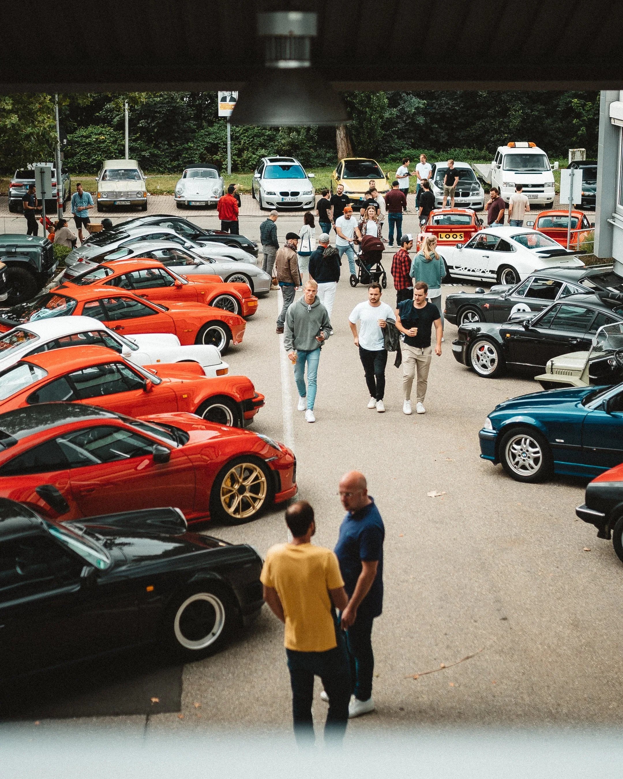 Blick auf eine Autoveranstaltung mit verschiedenen klassischen und Sportwagen sowie Menschen, die den Event besuchen, im Freien bei Tageslicht.