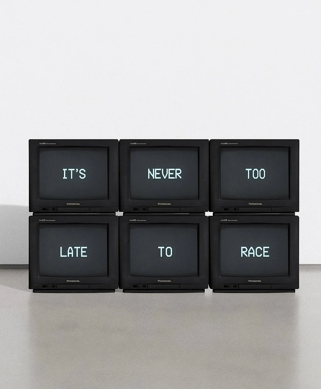 Sechs alte Monitore in zwei Reihen, die zusammen den Satz 'IT'S NEVER TOO LATE TO RACE' anzeigen.