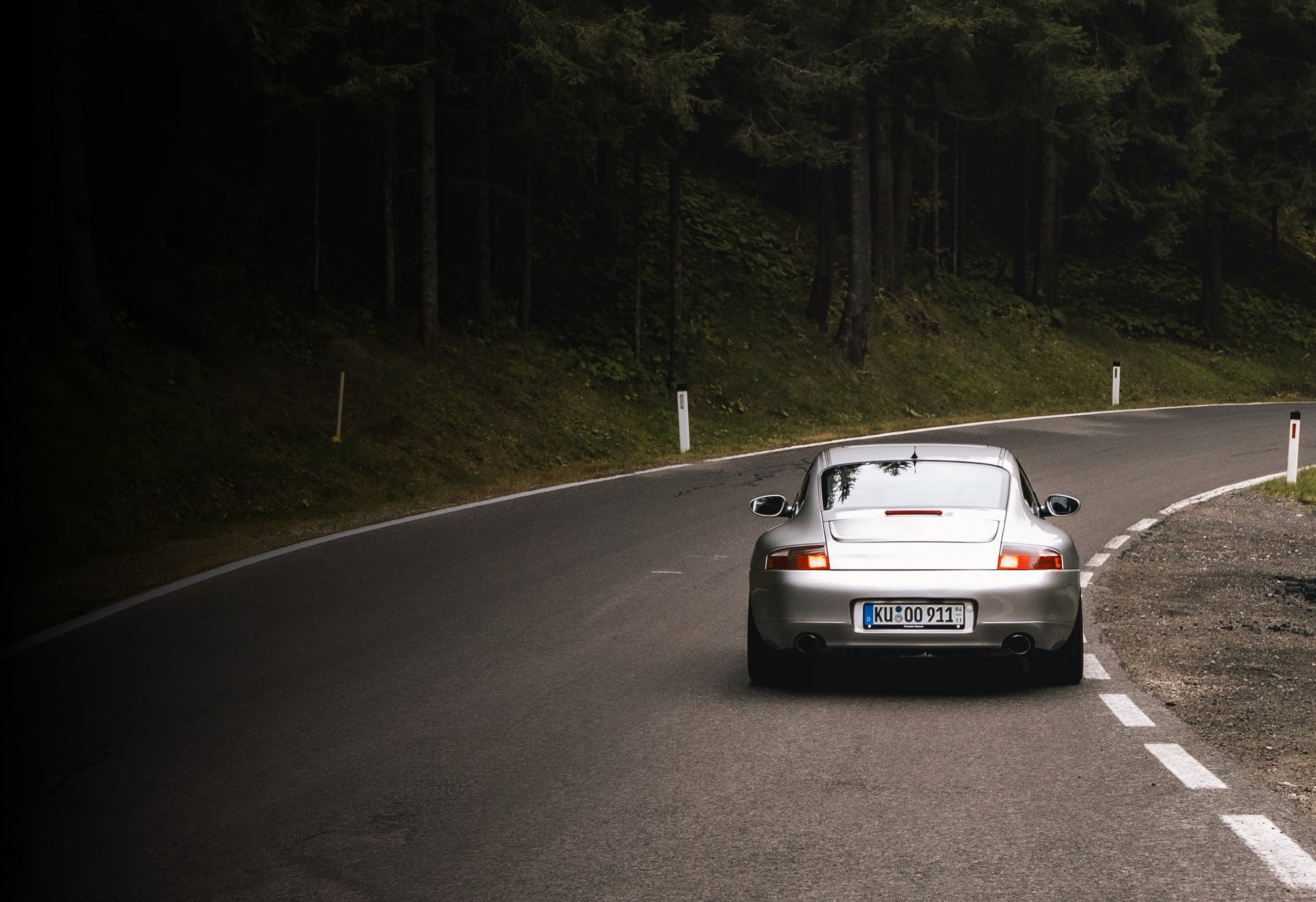 Silberner Porsche 911 fährt auf einer kurvigen Landstraße durch einen waldreichen Bereich in Deutschland.