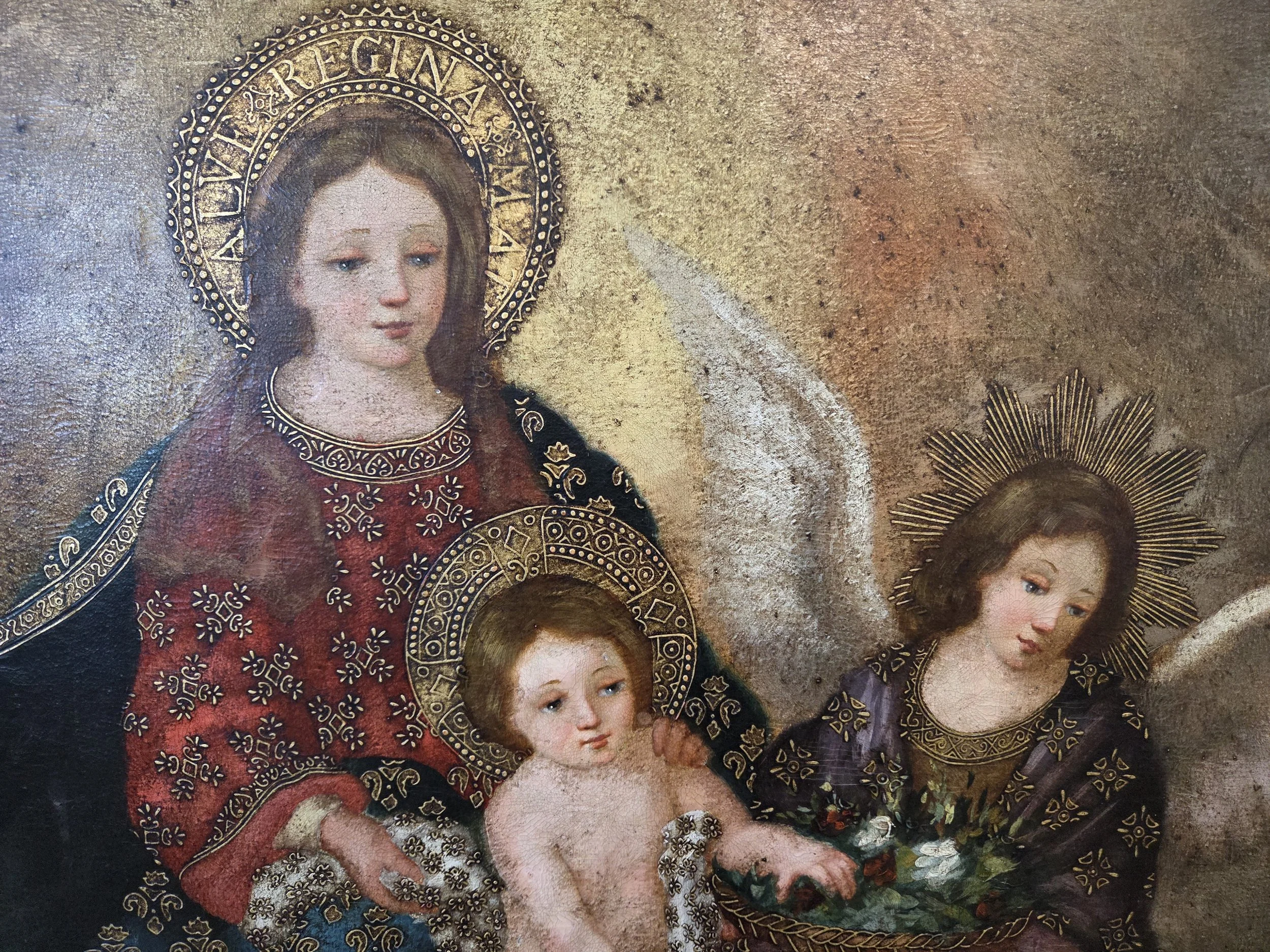 A religious painting depicting the Virgin Mary holding baby Jesus, with two angels on either side, all adorned with gold halos and intricate clothing.