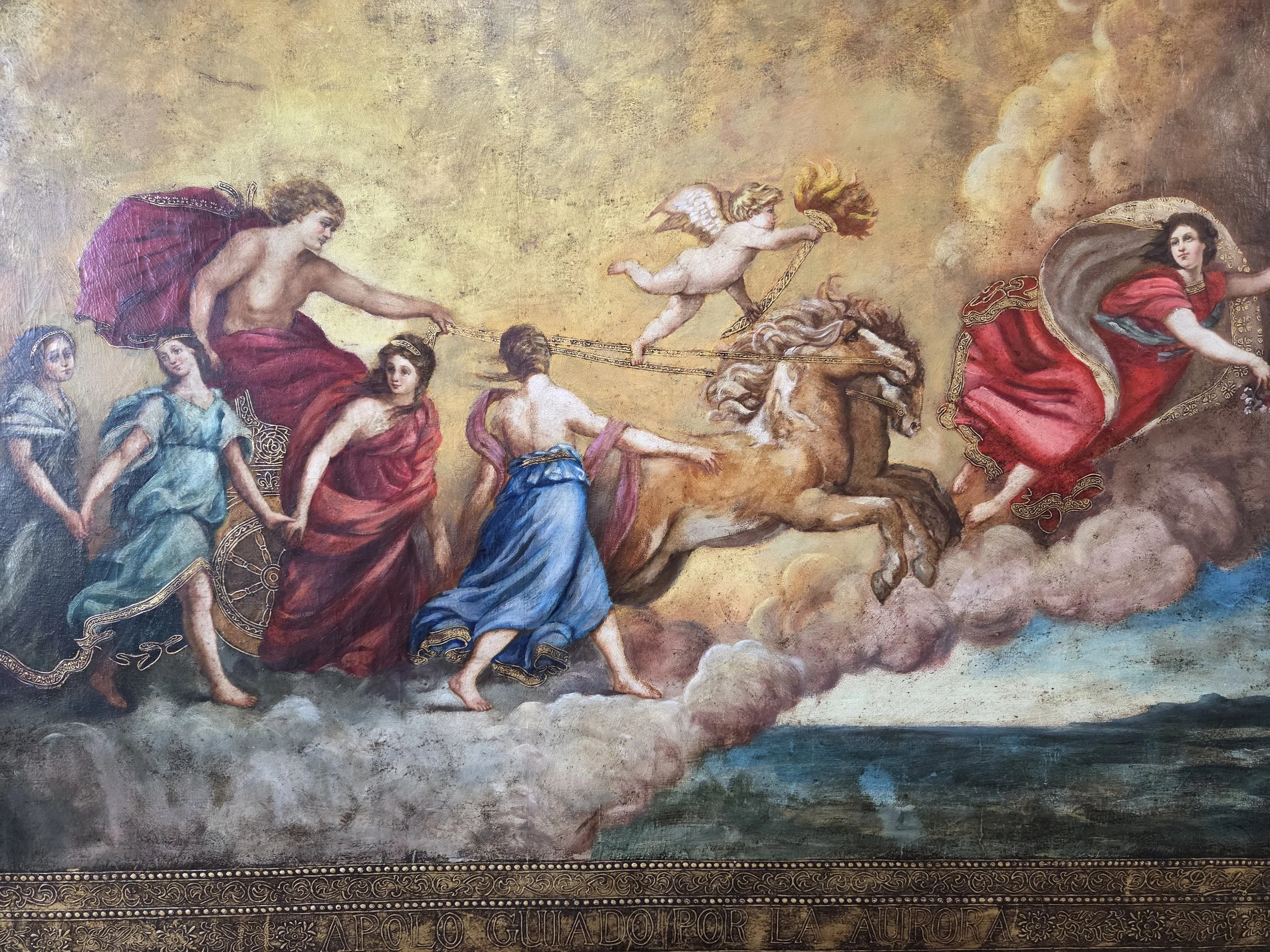 A classical painting depicting a mythological scene of gods riding chariots across the sky, led by a woman in red, with a cherub holding a torch nearby.