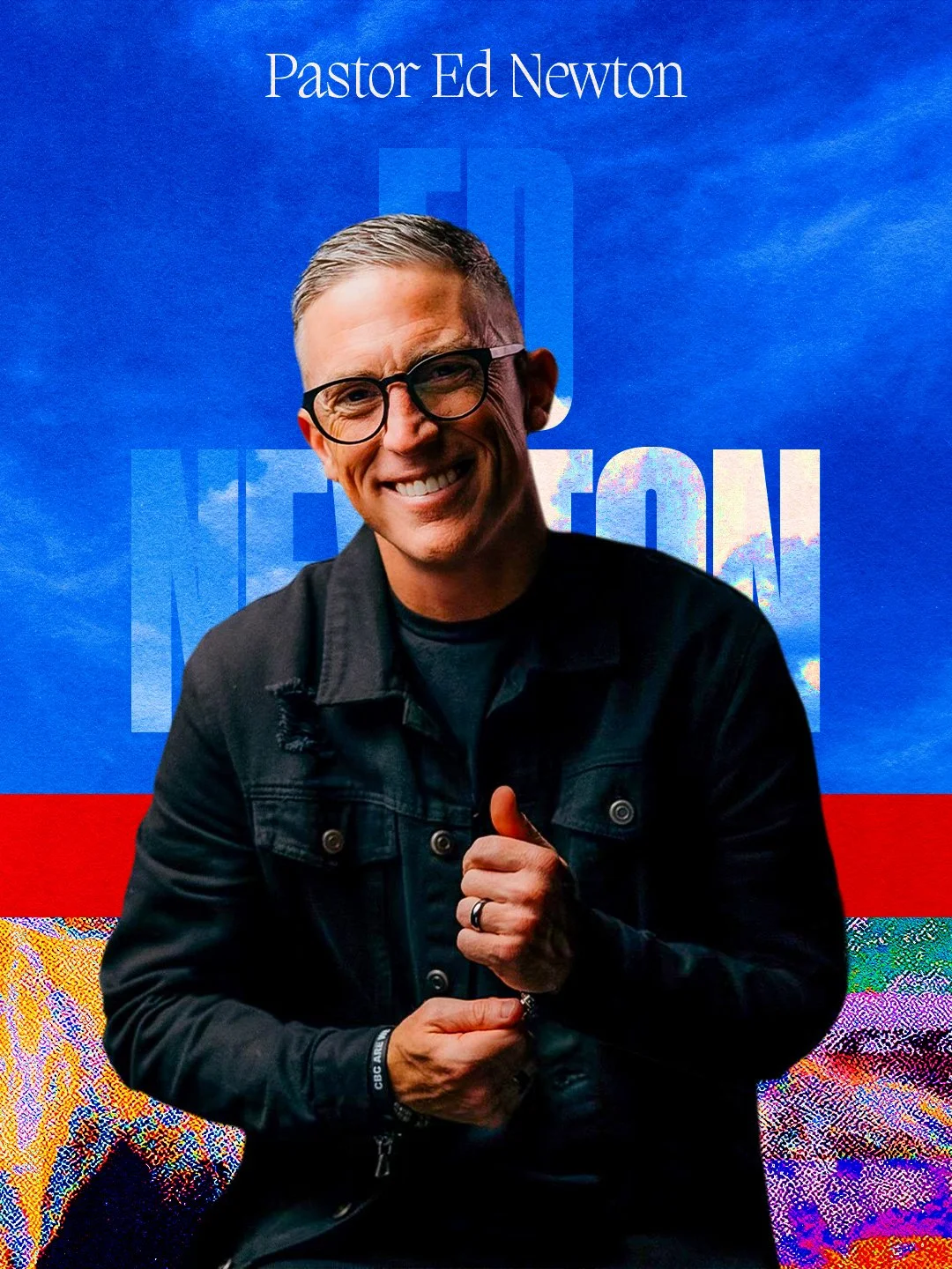 A man in a black hoodie and glasses speaking into a microphone while standing on stage with a dark background and subtle orange lighting.