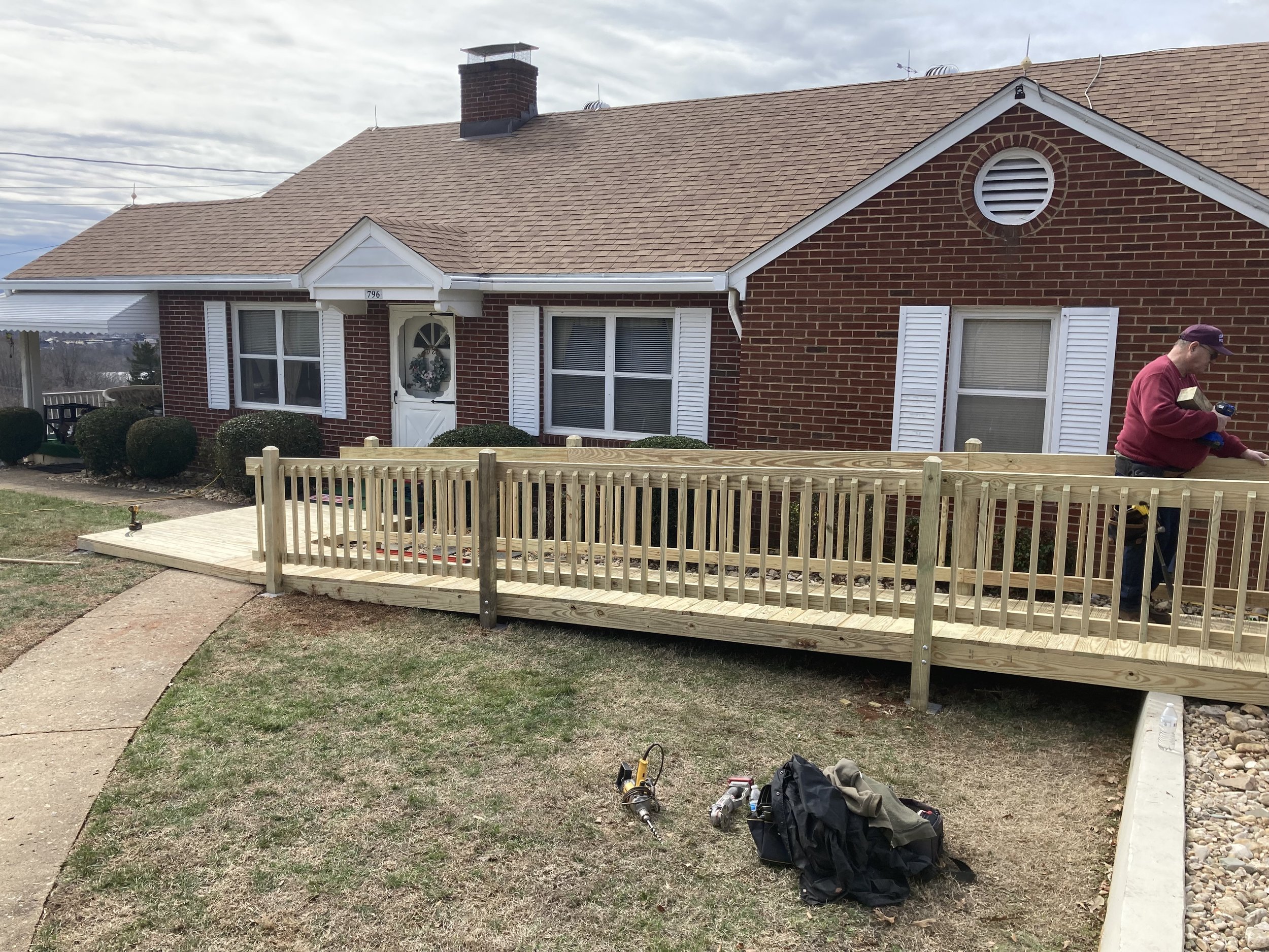 A man installing a wooden ramp in front of a red brick house with white shutters.