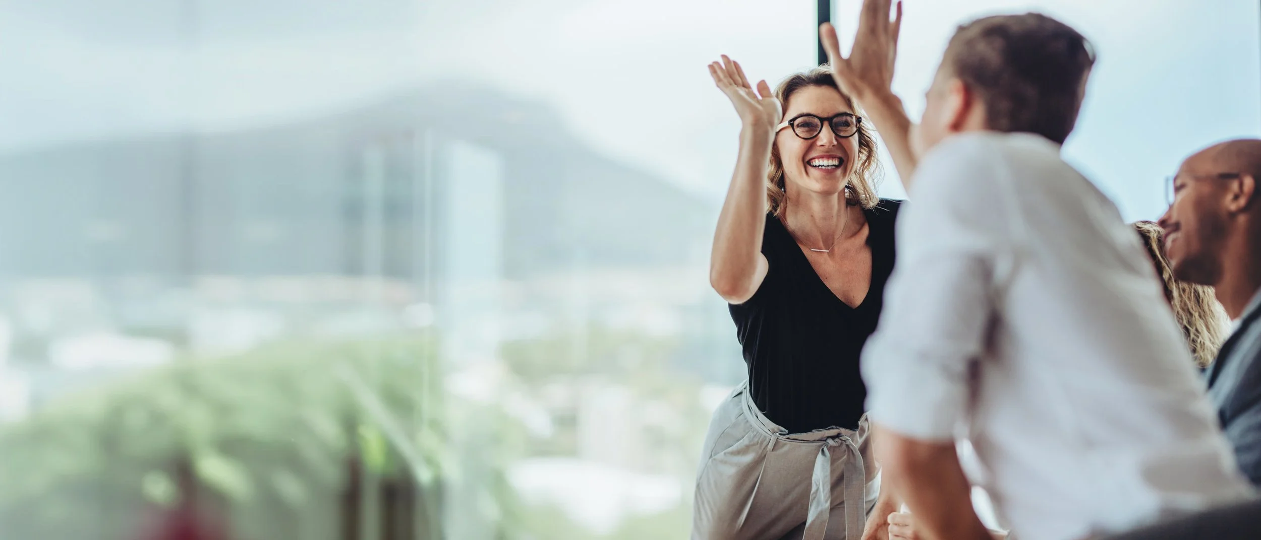 Women and men in a bright, modern office celebrating and giving high fives.