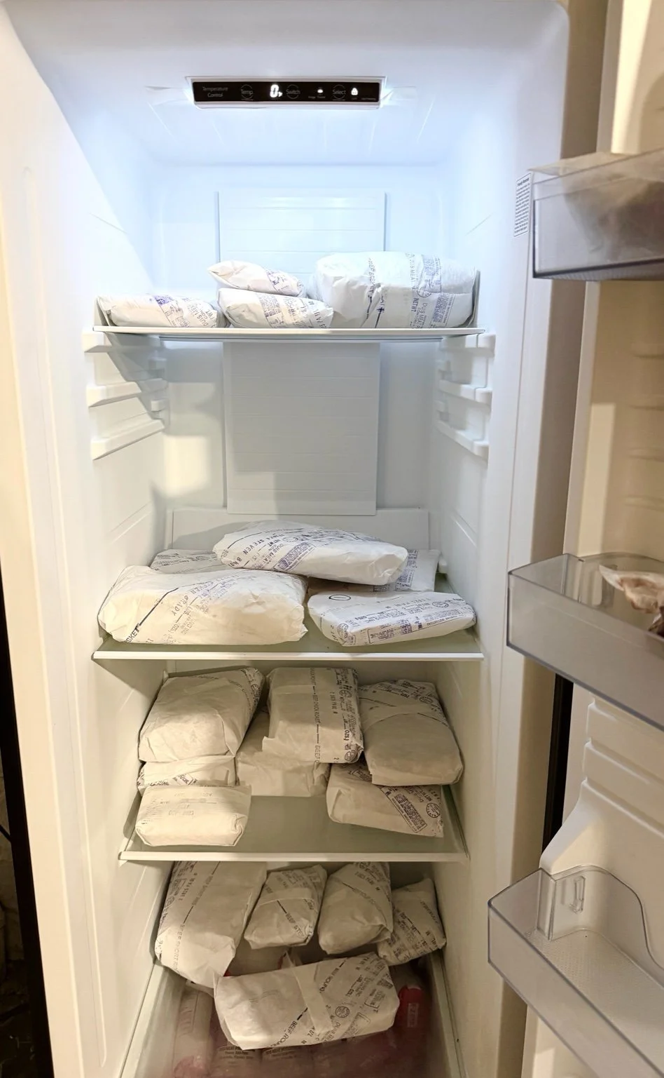 Inside of a freezer with multiple packages of beef wrapped in white paper on shelves.
