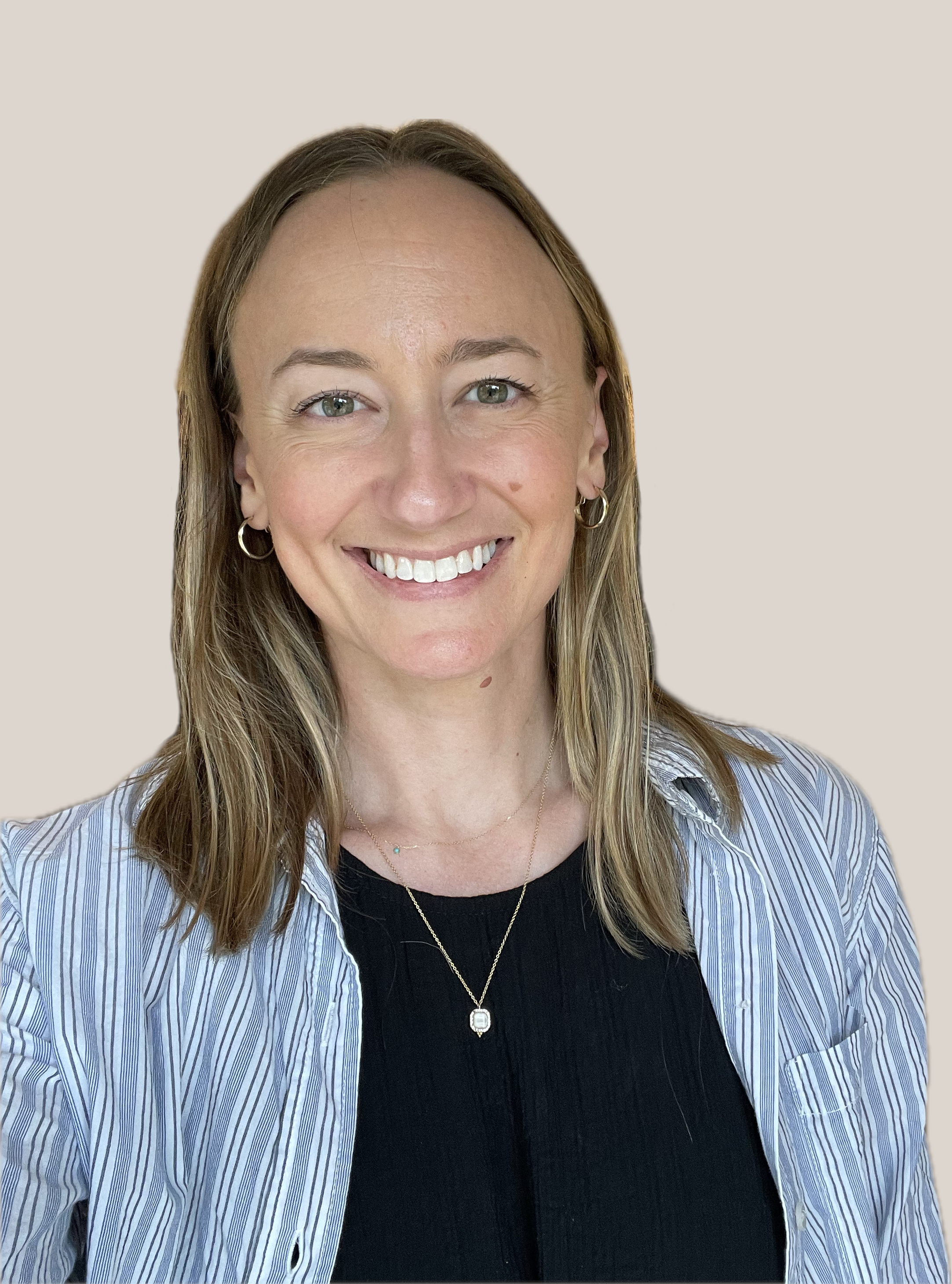 A woman with shoulder-length light brown hair, light skin, wearing a striped button-up shirt over a black top, smiling with white teeth, wearing small hoop earrings and a layered necklace with a pendant.
