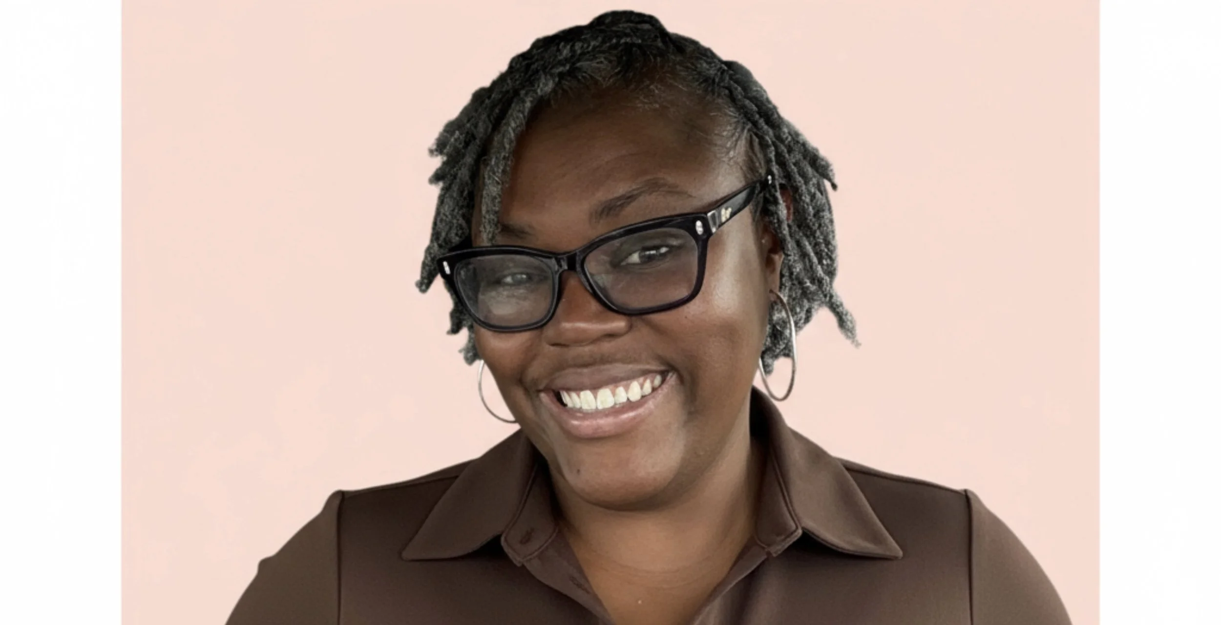 Portrait of Nae, creator of Nae in Bloom, smiling and wearing glasses and hoop earrings in a warm, natural setting.