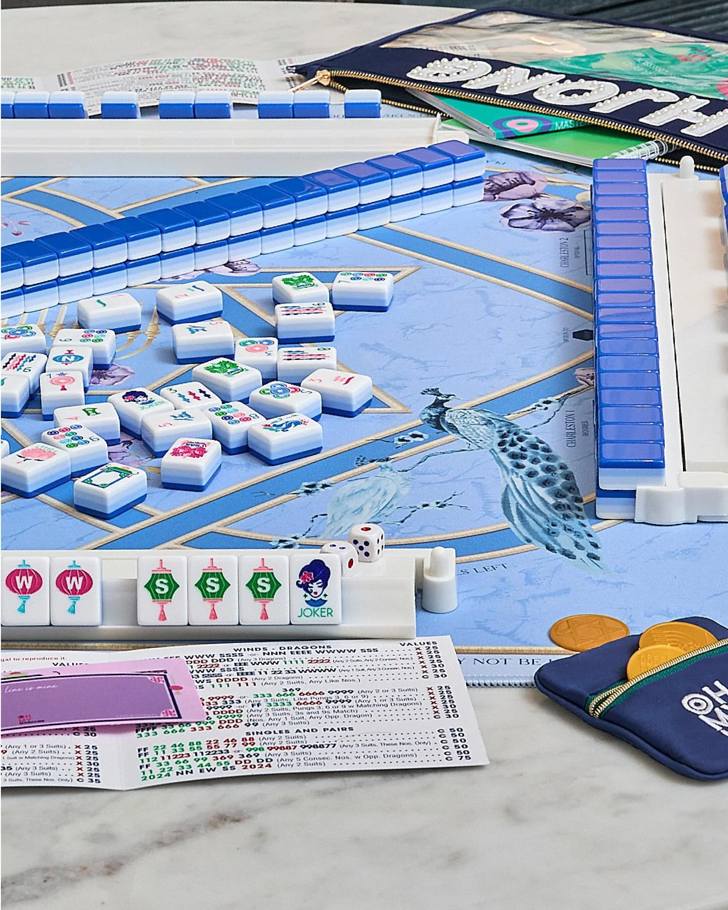 Close-up of a colorful Mahjong game in progress on a table with tiles, dice, and score sheets, on a marble surface.