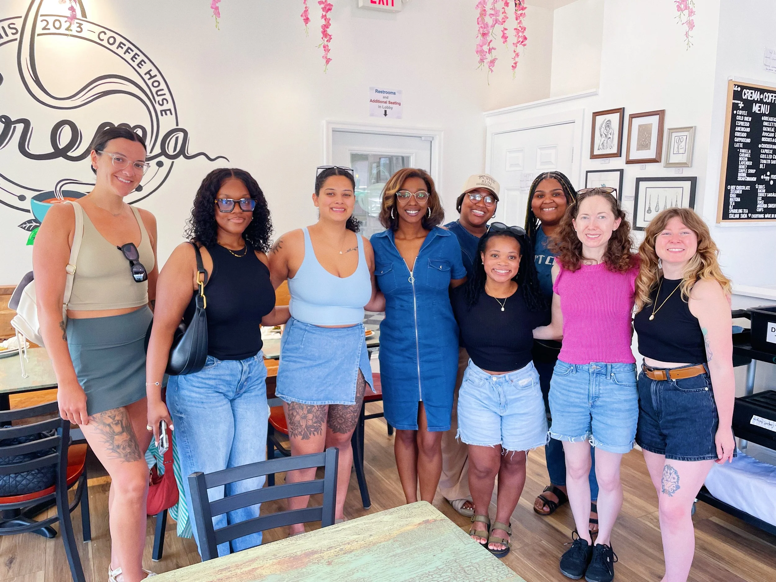 A group of ten women standing together inside a coffee shop, smiling at the camera.