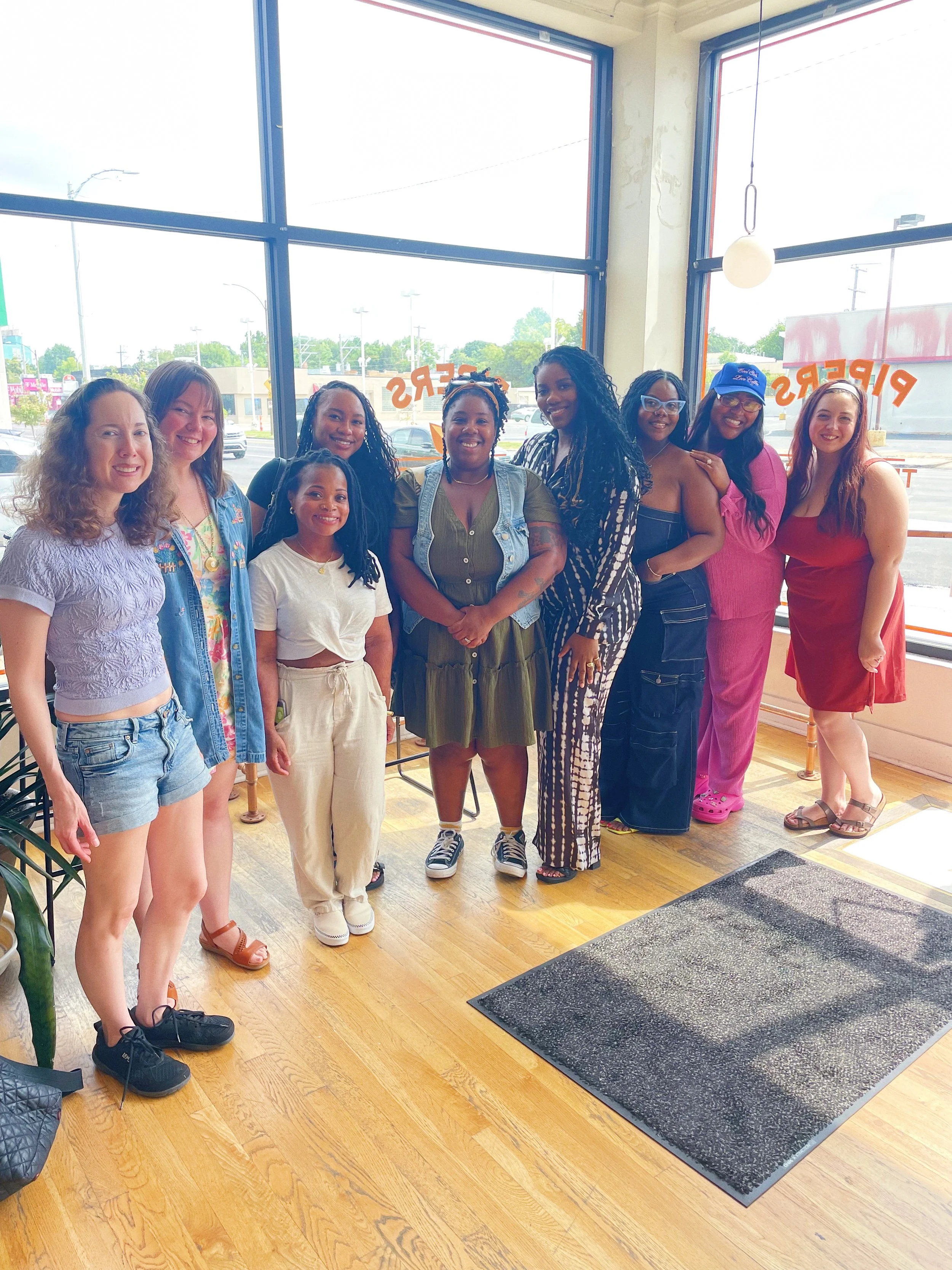 Group of nine women standing together inside a restaurant, posing for a photo.
