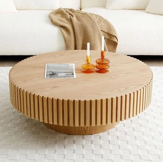 Living room design Inspiration featuring a stylish shoppable Round wooden coffee table with two amber-colored glass candlesticks, a magazine, and a beige blanket draped over a white sofa.