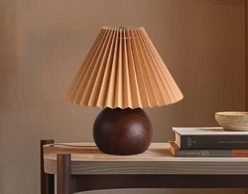Interior design Inspiration featuring a stylish shoppable table lamp with a pleated paper shade and a round dark base, placed on a wooden surface with a stack of books nearby.
