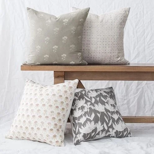 Living room design Inspiration featuring a stylish shoppable  decorative pillows with various patterns and colors, arranged on and in front of a wooden bench against a white fabric background.