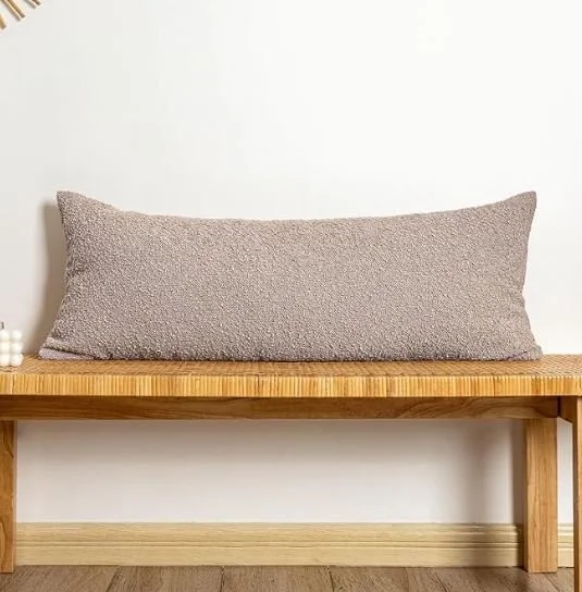 Bedroom design Inspiration featuring a stylish shoppable beige textured pillow resting on a wooden bench against a white wall.